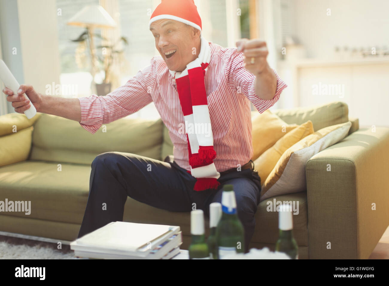 Begeisterte reifer Mann in Hut und Schal vor dem Fernseher Sportveranstaltung auf Sofa im Wohnzimmer Stockfoto