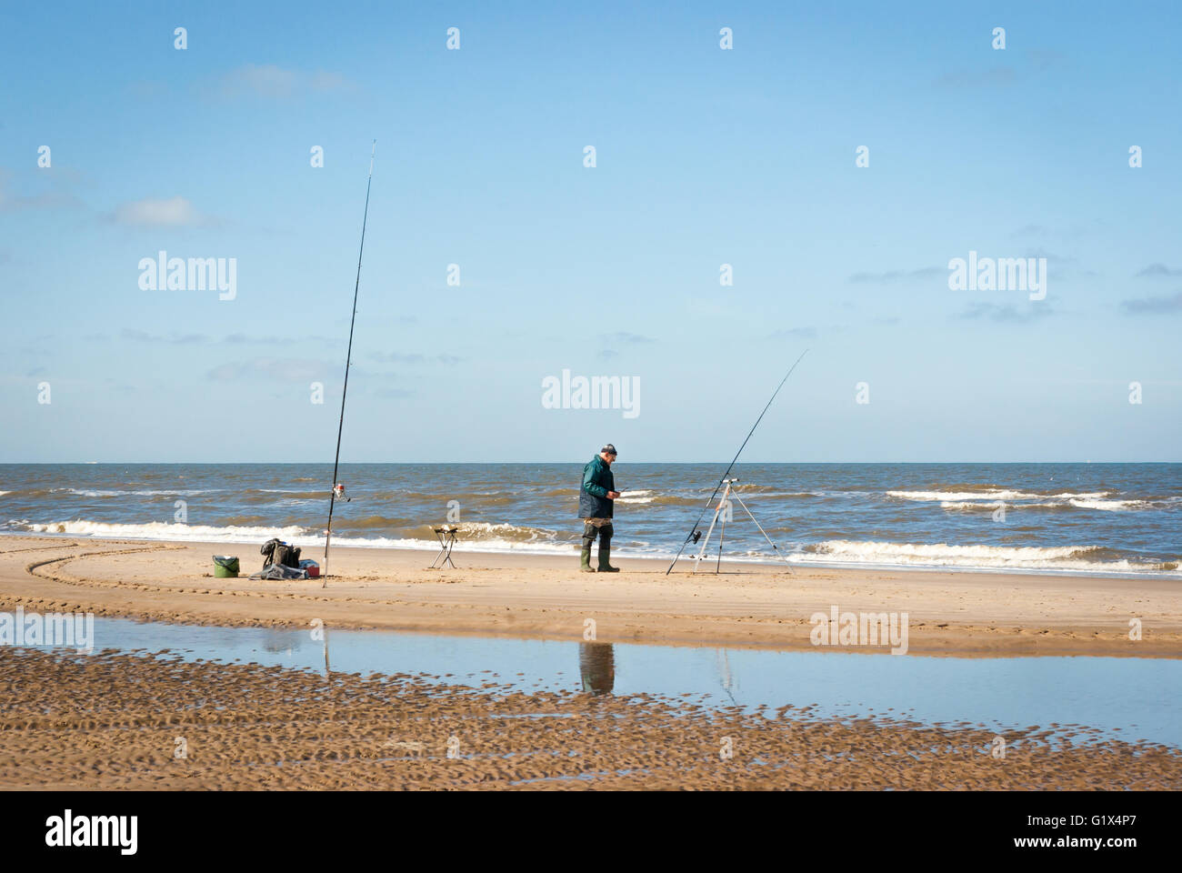 Ein Fischer-Mann mit zwei Angelruten am Nordseestrand im Meer-Angelwettbewerb in Egmond-Aan-Zee Niederlande Stockfoto