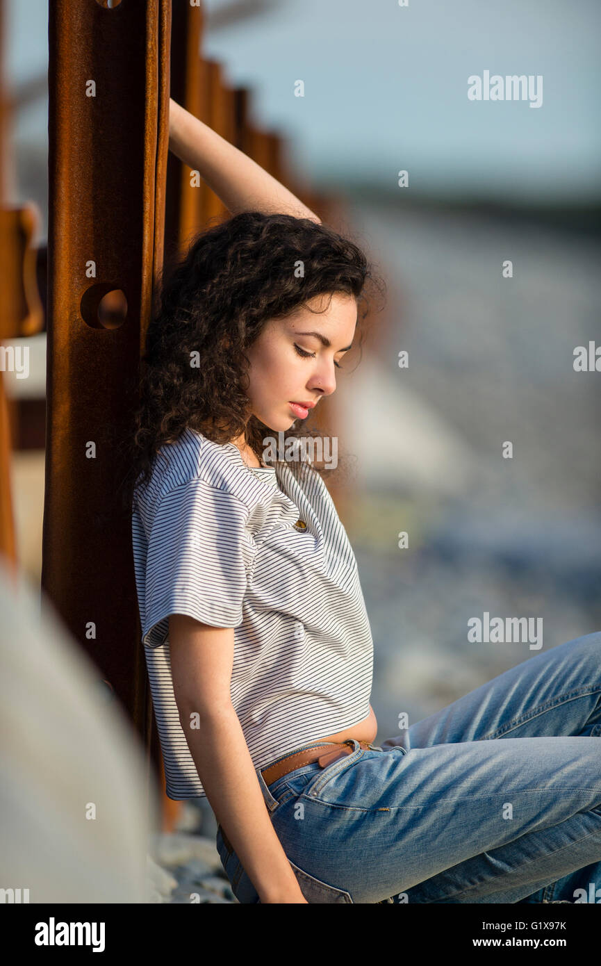 Eine junge attraktive schlanke Brünette Frau Mädchen tief in dachte, allein, allein, im freien außerhalb an einem warmen Abend. UK Stockfoto