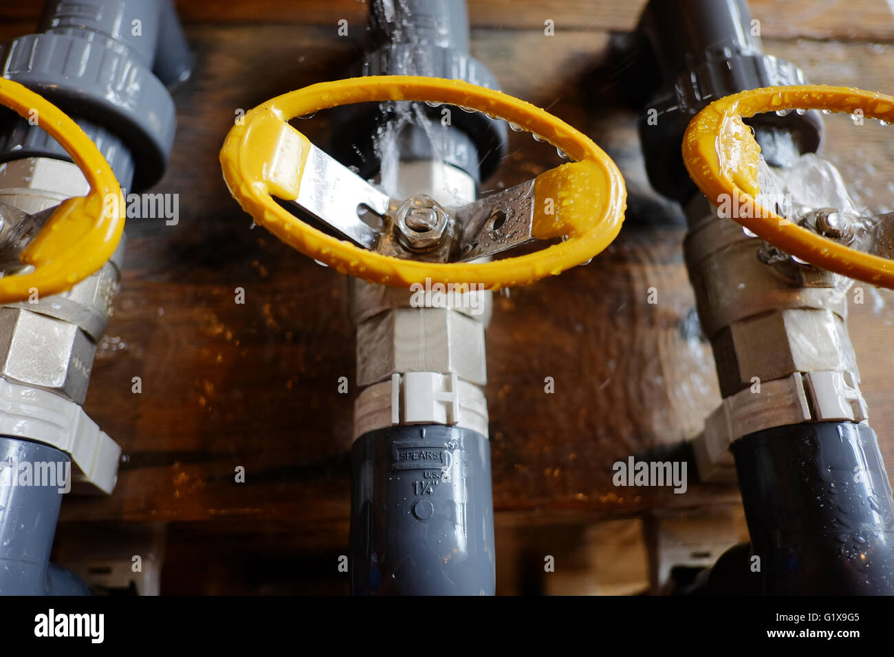 Leuchtend gelbe Ventile auf PVC Wasserleitungen aus Holz im Hintergrund. Stockfoto