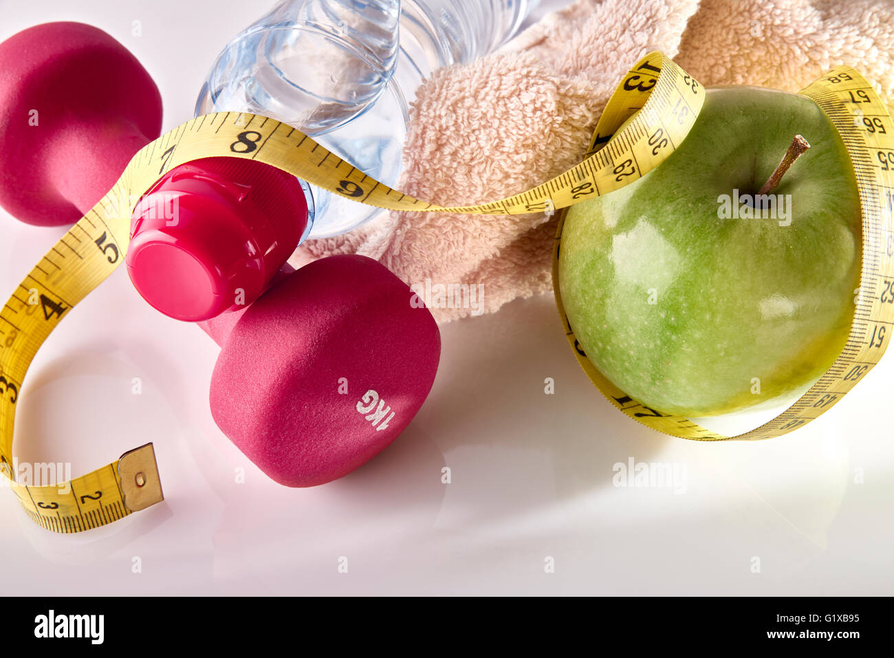 Hanteln mit Apfel und Maßband auf weißem Glastisch und isolierten Hintergrund. Konzept Frauen Lifestyle, Gesundheit, Ernährung Stockfoto