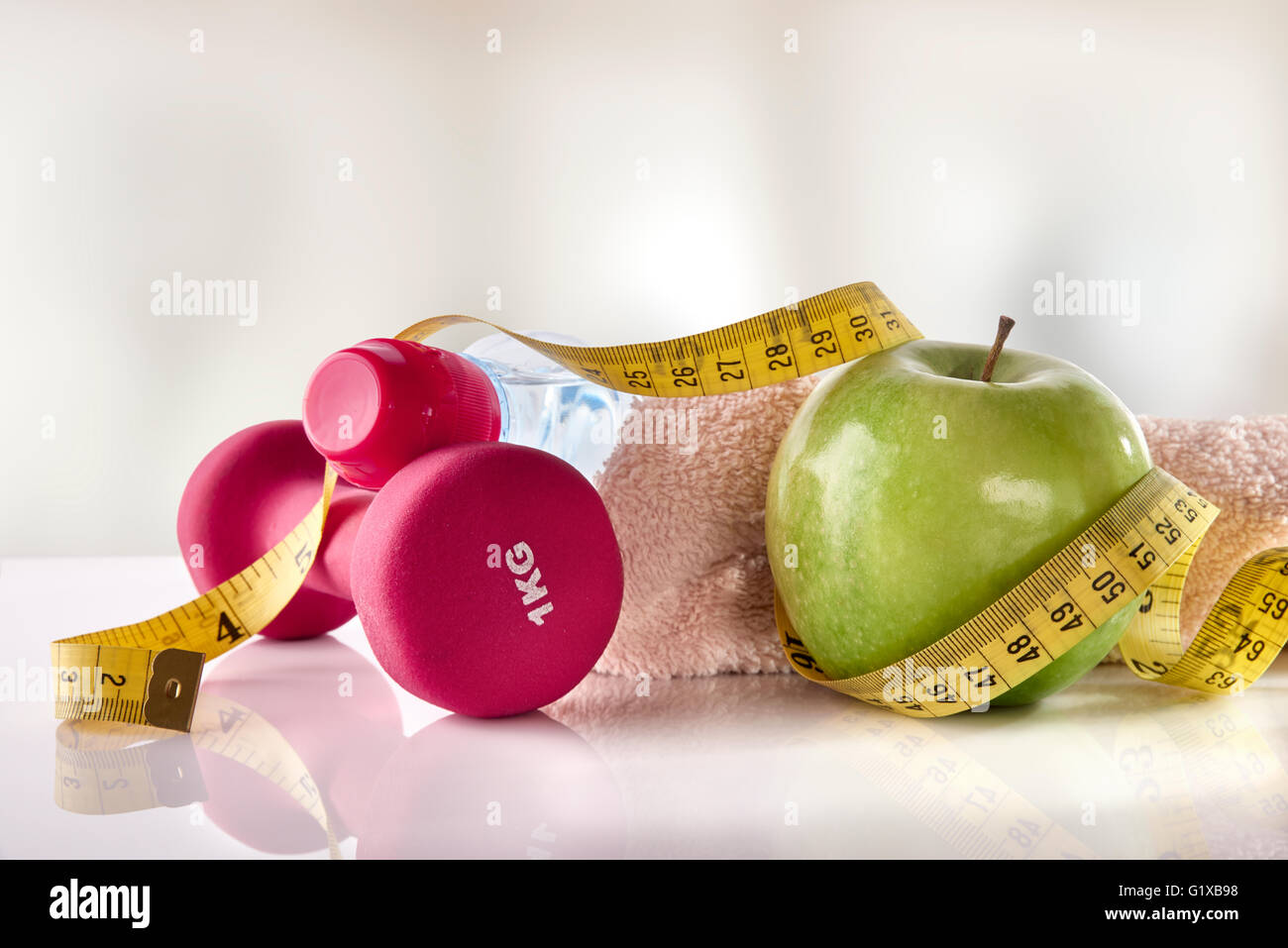 Hanteln mit Apfel und Maßband auf weißem Glas Tisch und Fitness-Studio-Hintergrund. Konzept-Frauen-Lifestyle, Gesundheit, Ernährung und Sport. Stockfoto