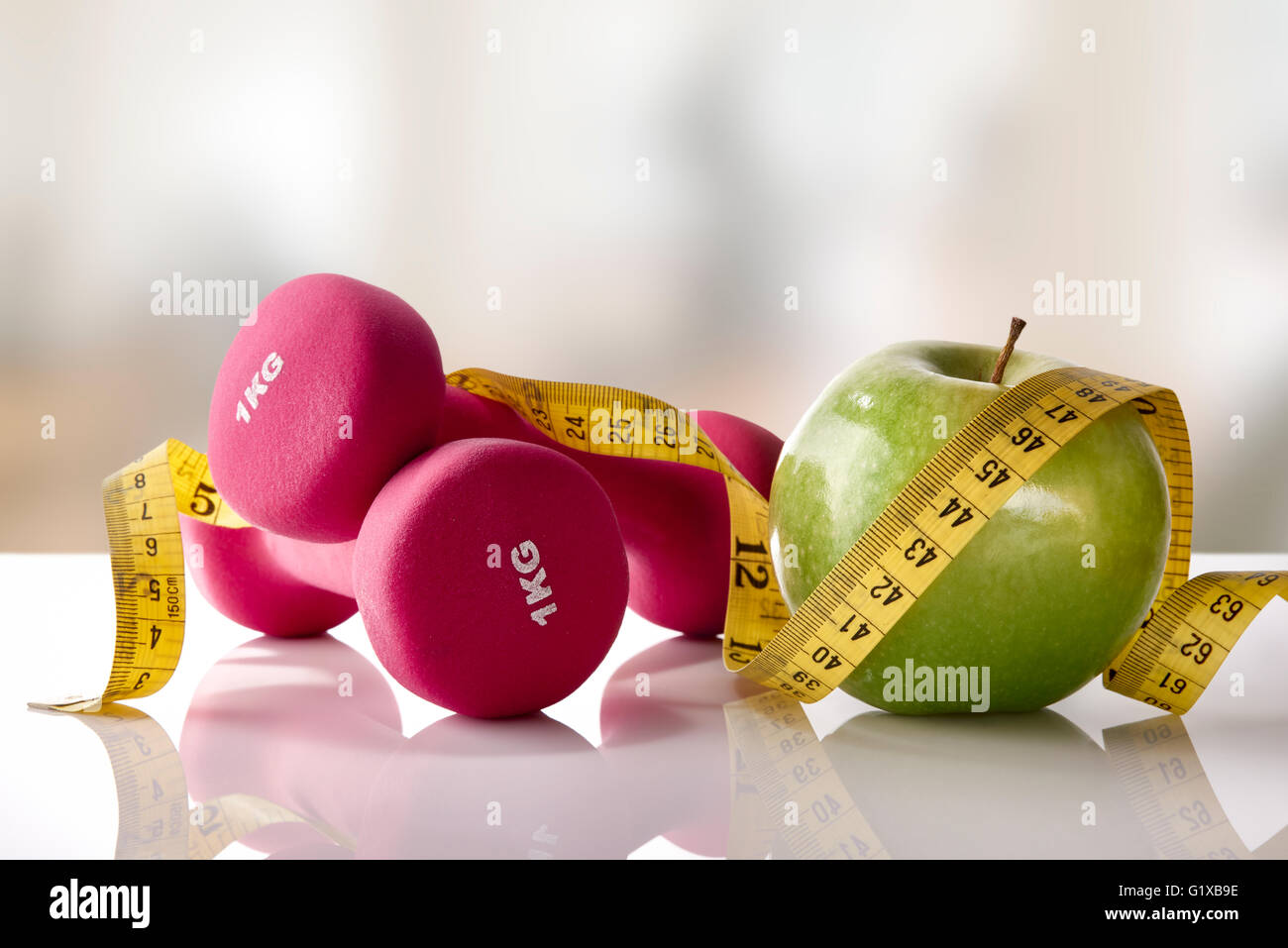 Hanteln mit Apfel und Maßband auf weißem Glas Tisch und Fitness-Studio-Hintergrund. Konzept-Frauen-Lifestyle, Gesundheit, Ernährung und Sport. Stockfoto