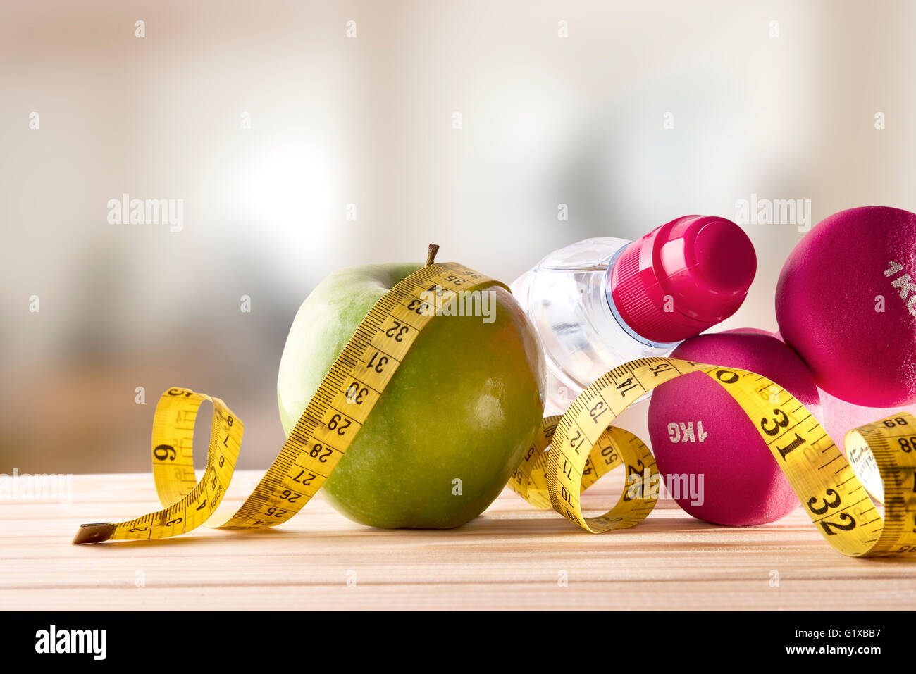 Hanteln mit Apfel, Mineralwasserflasche und Maßband auf Holz Tisch und Fitness-Studio-Hintergrund. Konzept Frauen Lifestyle, Gesundheit Stockfoto