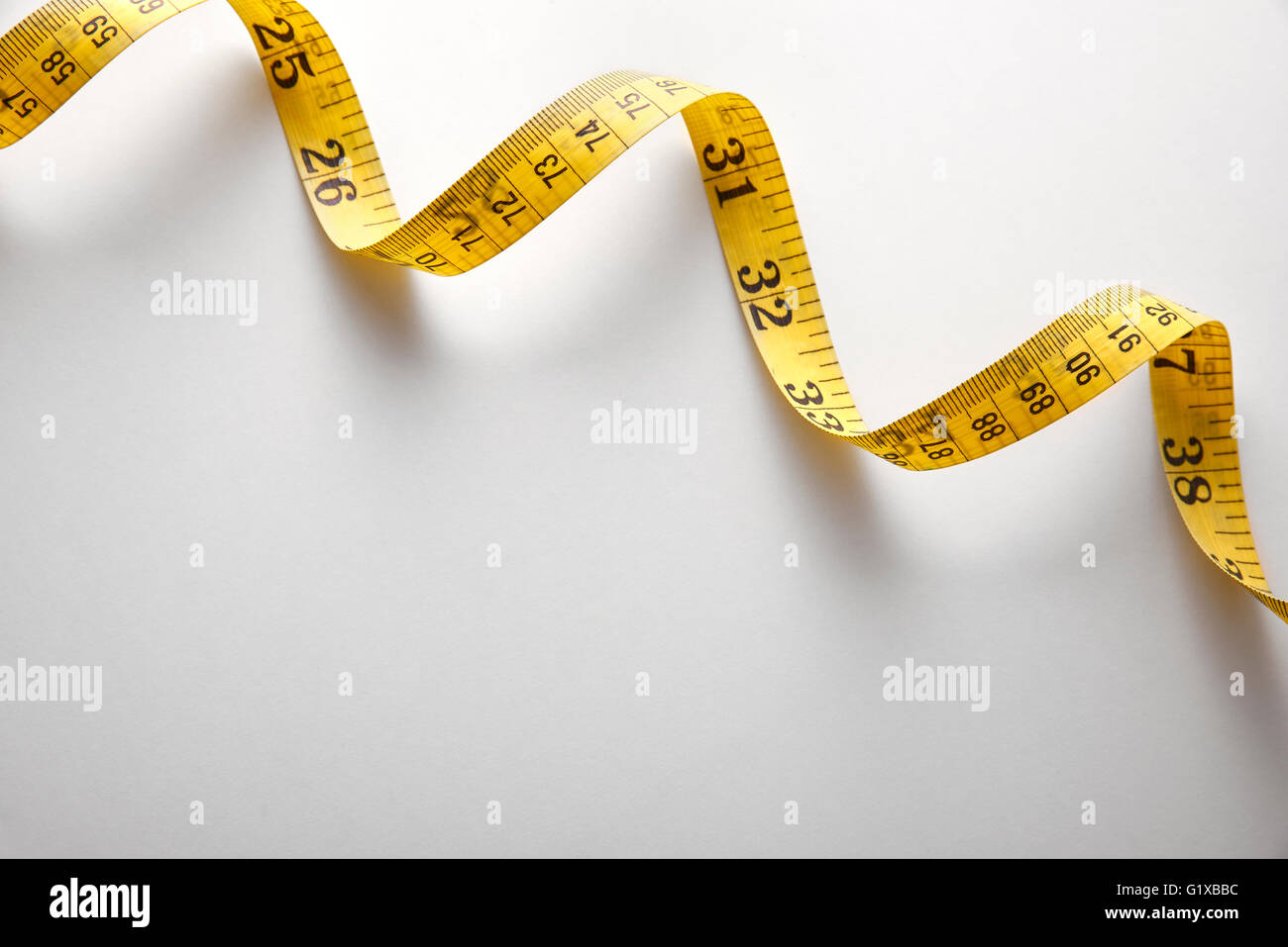 Gelben Maßband in Meter und Zoll in einer Spirale auf weißen Tisch. Ansicht von oben. Horizontale Komposition. Stockfoto