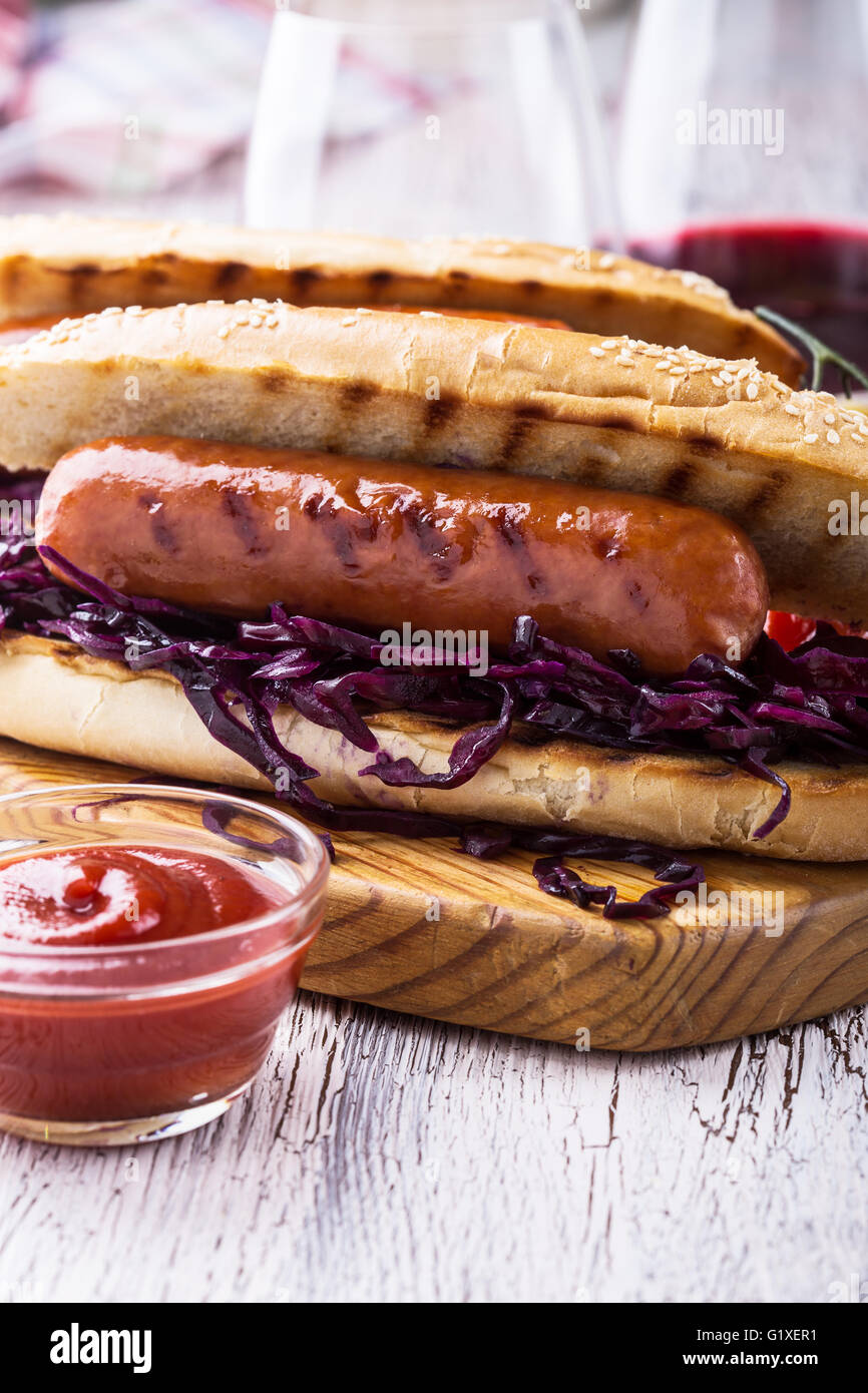 Grillwurst-Sandwich mit süßen Rotkohl Krautsalat, Senf und Tomatensauce auf Holzbrett Stockfoto