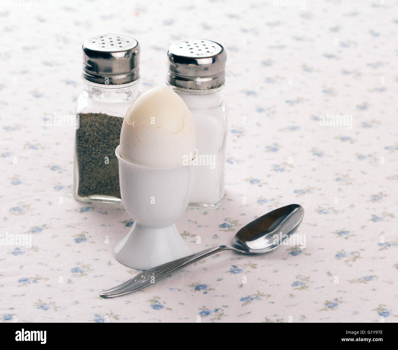 Ei in einen Eierbecher mit Löffel, Salz- und Pfefferstreuer auf eine alte altmodische Tischdecke Stockfoto