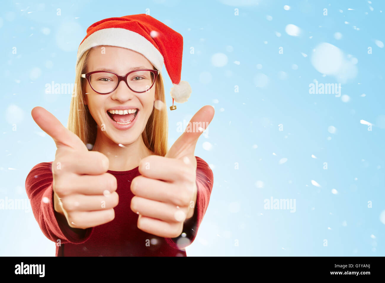 Lächelnde junge, blonde Frau mit Daumen oben im Schnee zu Weihnachten Stockfoto