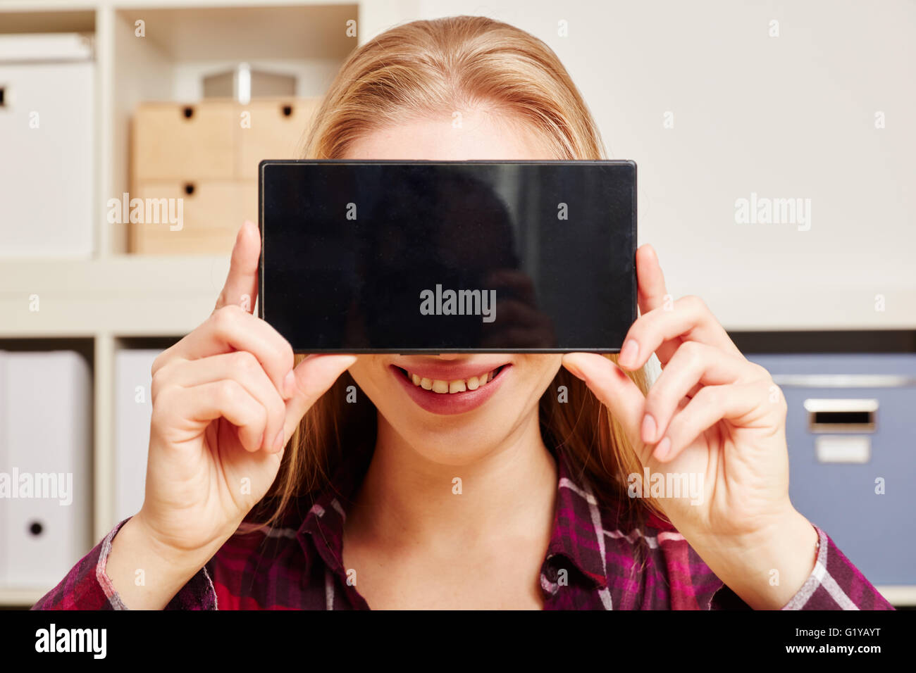 Lächelnde Frau hält eine Smartphone mit einem schwarzen Touchscreen vor den Kopf Stockfoto