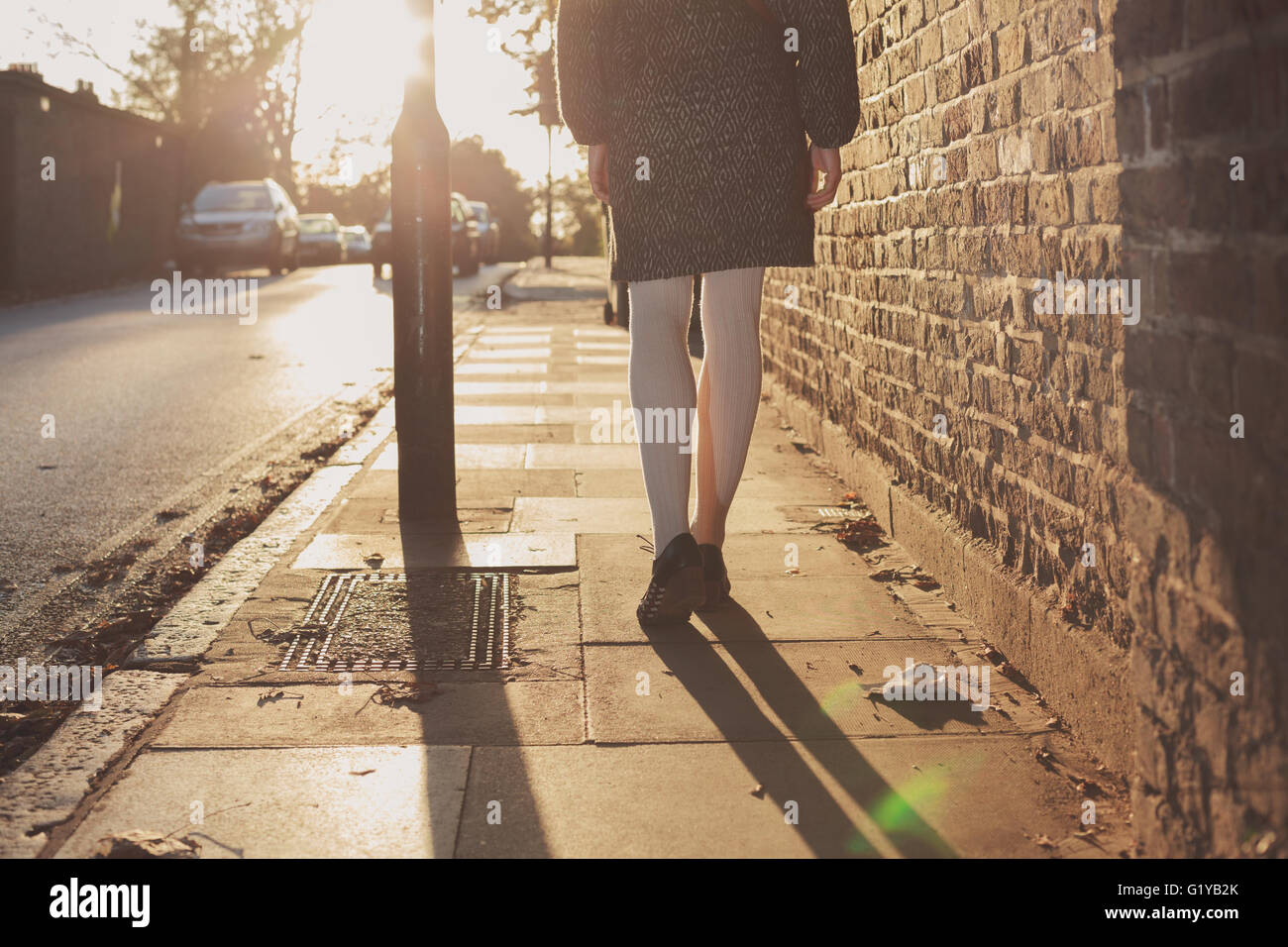 Eine junge Frau geht in den Sonnenuntergang an einem Herbsttag in der Stadt spazieren. Stockfoto