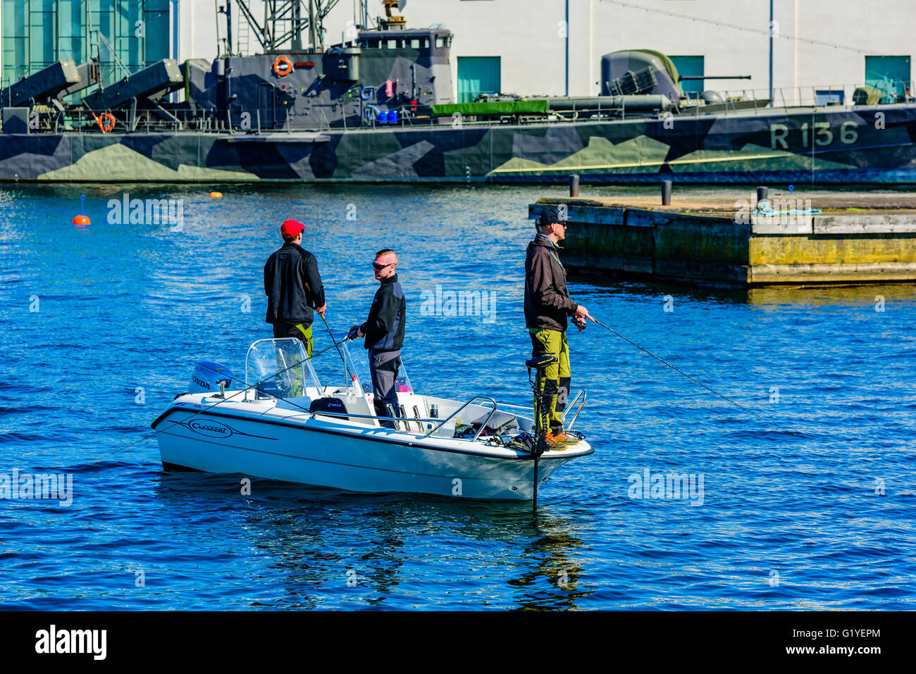 Karlskrona, Schweden - 5. Mai 2016: Drei junge Erwachsene Männer stehen in einem Halbmond Motorboot Angeln mit Rute und Tackle im Hafen. Stockfoto