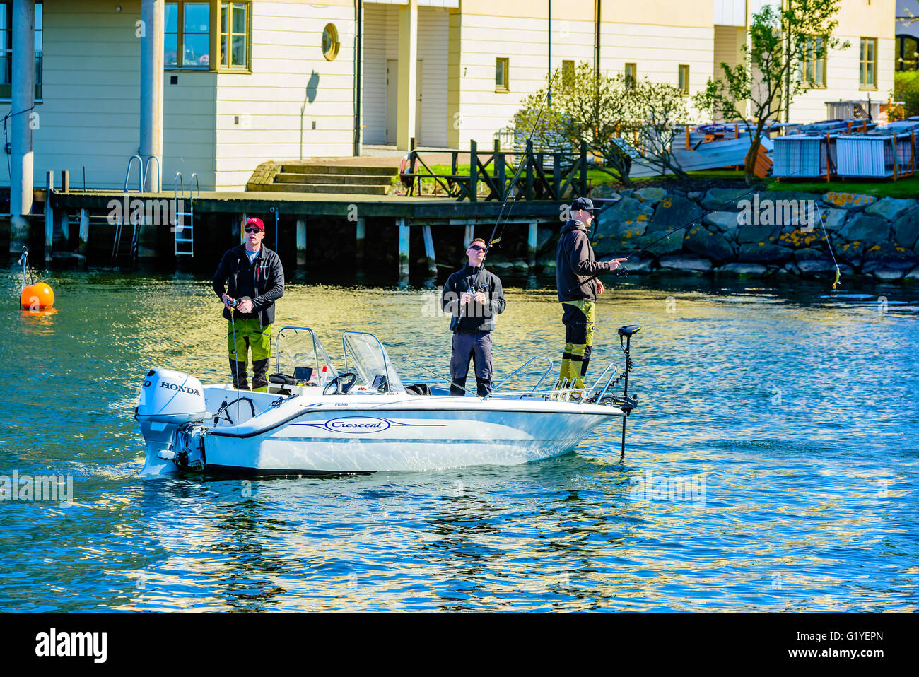 Karlskrona, Schweden - 5. Mai 2016: Drei junge Erwachsene Männer stehen in einem Halbmond Motorboot Angeln mit Rute und Tackle im Hafen. Stockfoto