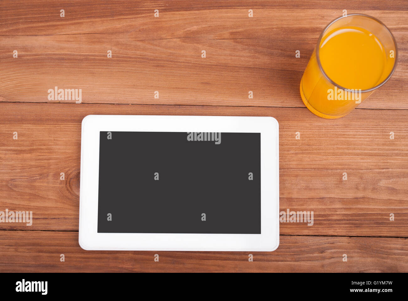 Digital-Tablette und ein Glas Orangensaft auf einem Holztisch. Stockfoto