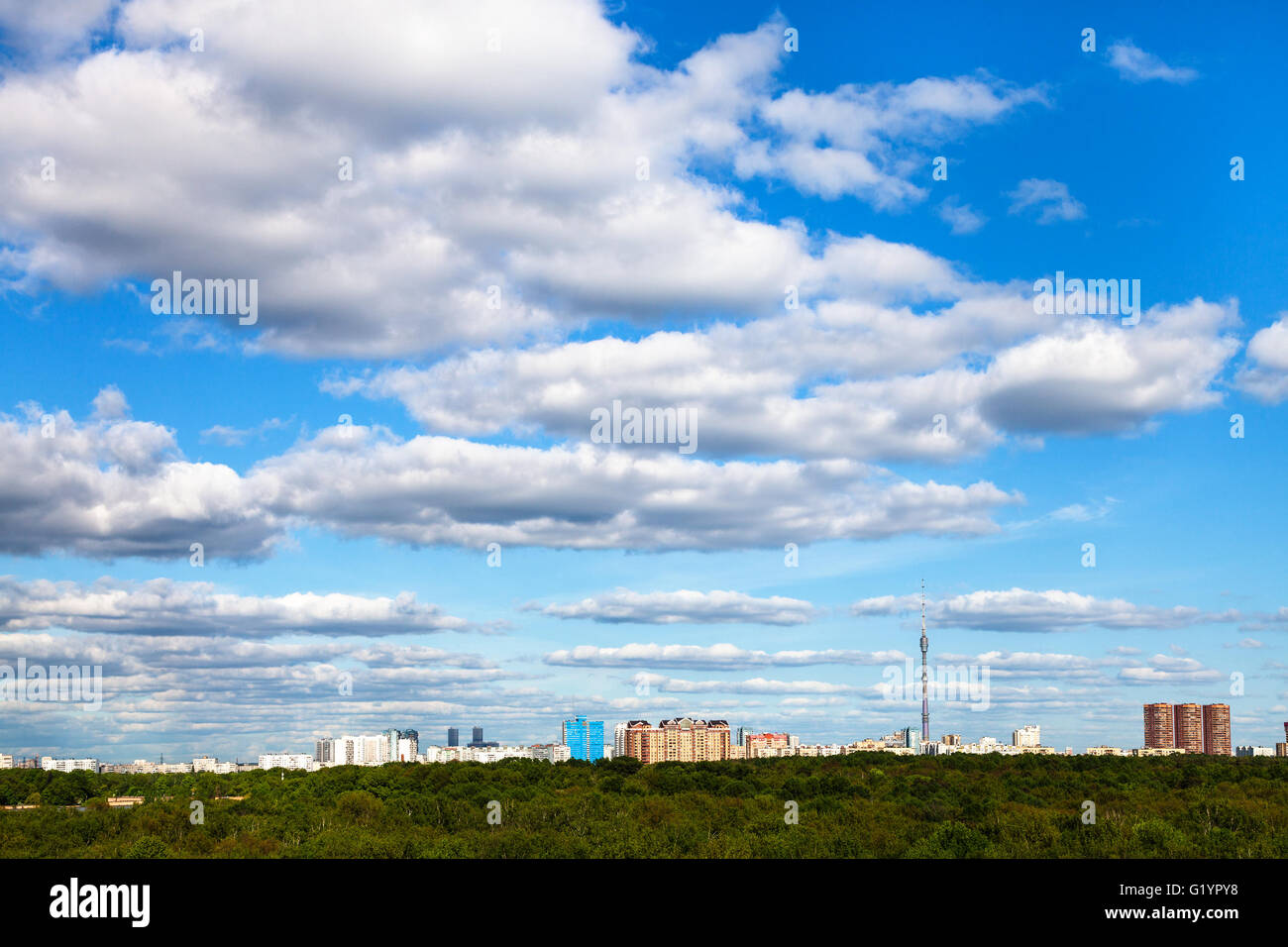 weiße Wolken am blauen Himmel über Stadt und grün Wald am sonnigen Sommertag Stockfoto