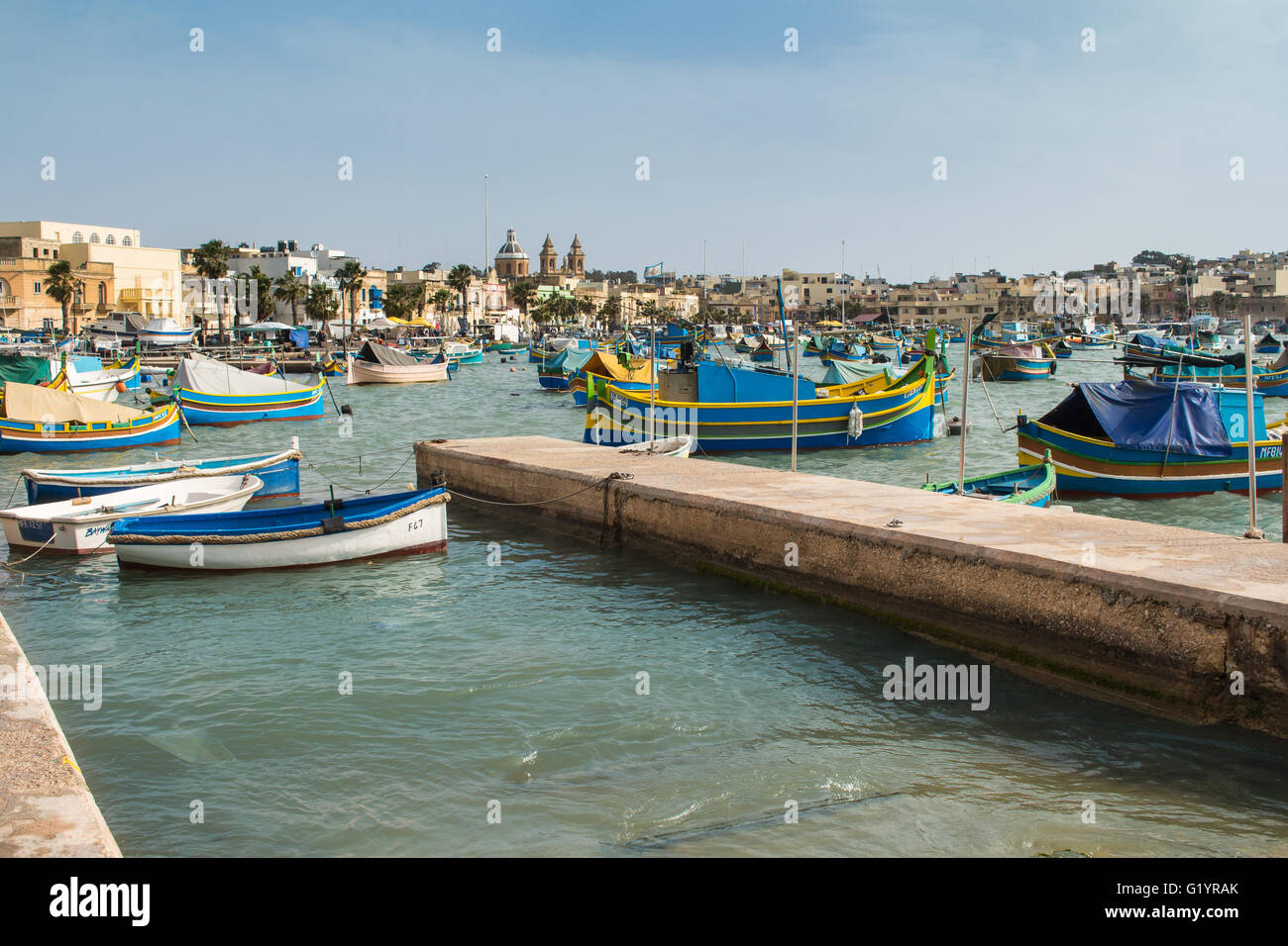 Traditionelles Fischerdorf Marsaxlokk an der Insel Malta. Viele bunte Holzboote in der Bucht. Kirche im Hintergrund. Stockfoto