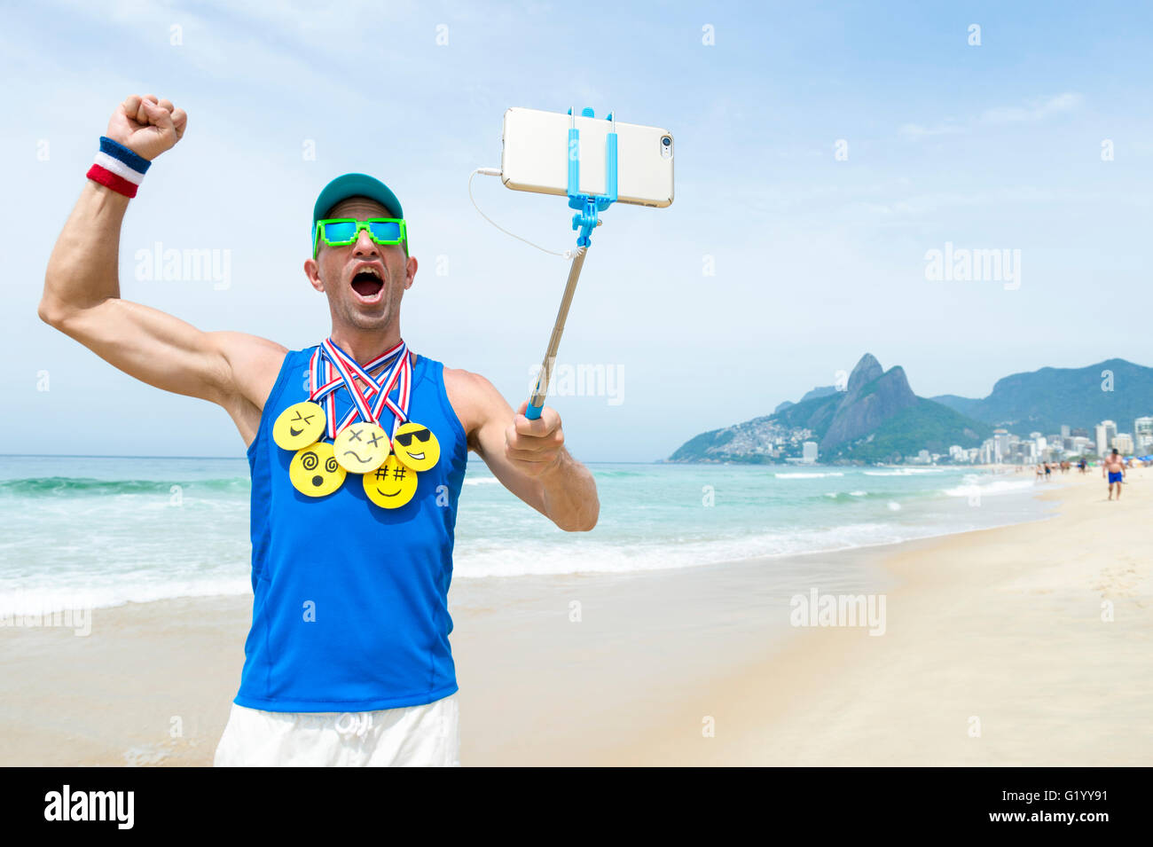 Sportler nehmen Selfie tragen Goldmedaillen mit hellen gelben Emoji Gesichter mit Smartphone auf Selfie Stick am Strand von Ipanema in Rio Stockfoto