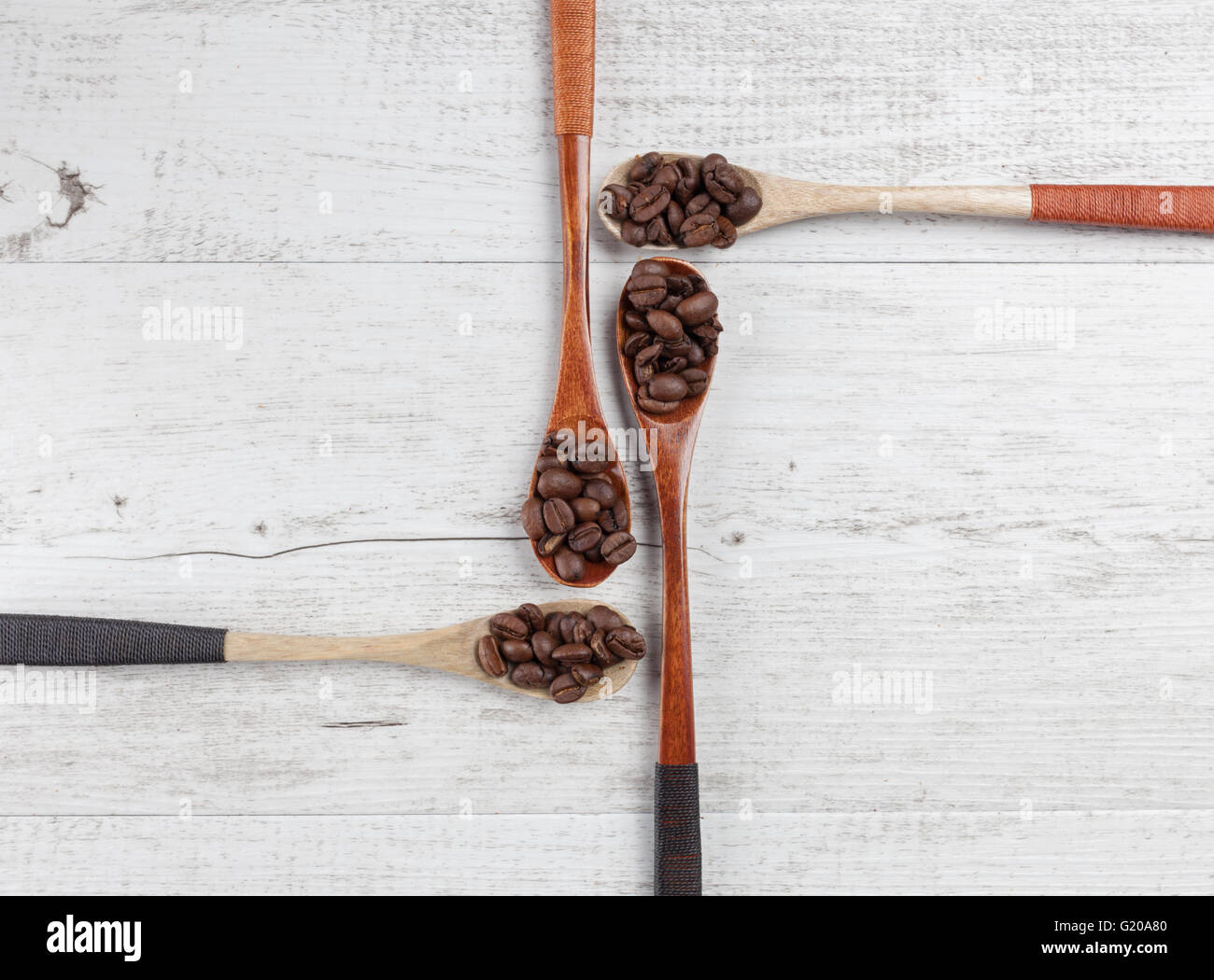 Vier hölzerne Löffel mit gerösteten Kaffeebohnen, die kreativ auf weißem rustikalen Holz angeordnet. Draufsicht mit Textfreiraum Stockfoto