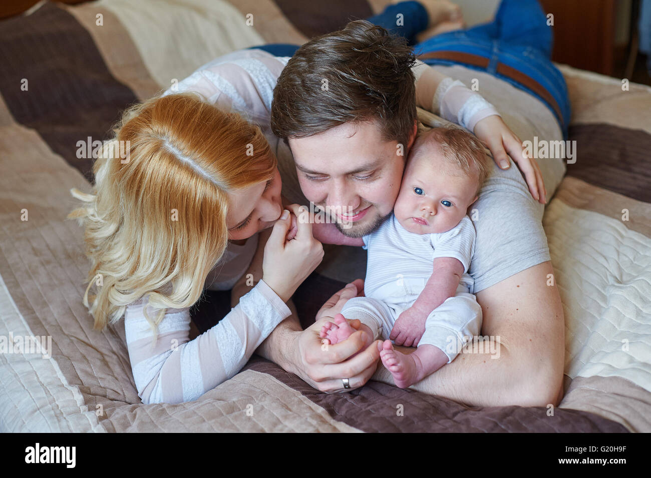 Schöne glückliche Paar und ihr Baby gemeinsam in einem Bett entspannen Stockfoto