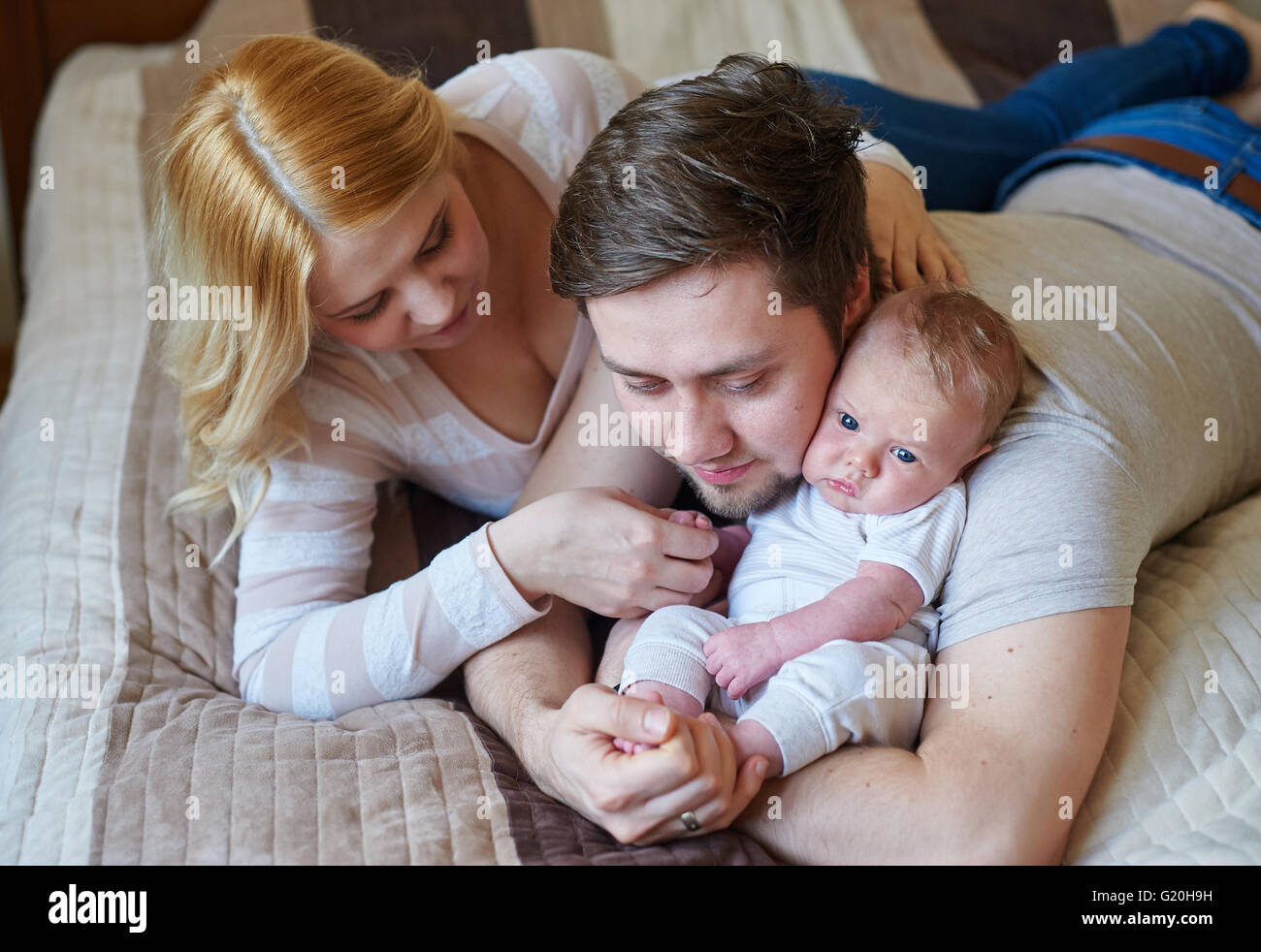 Schöne glückliche Paar und ihr Baby gemeinsam in einem Bett entspannen Stockfoto