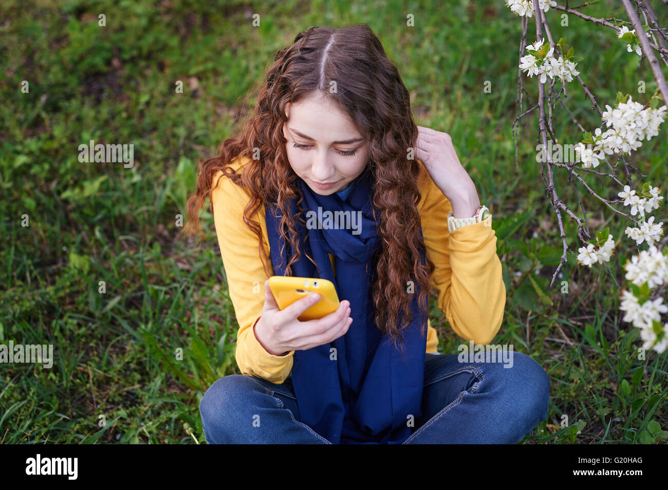 junge Frau im blühenden Frühlingsgarten mit smartphone Stockfoto