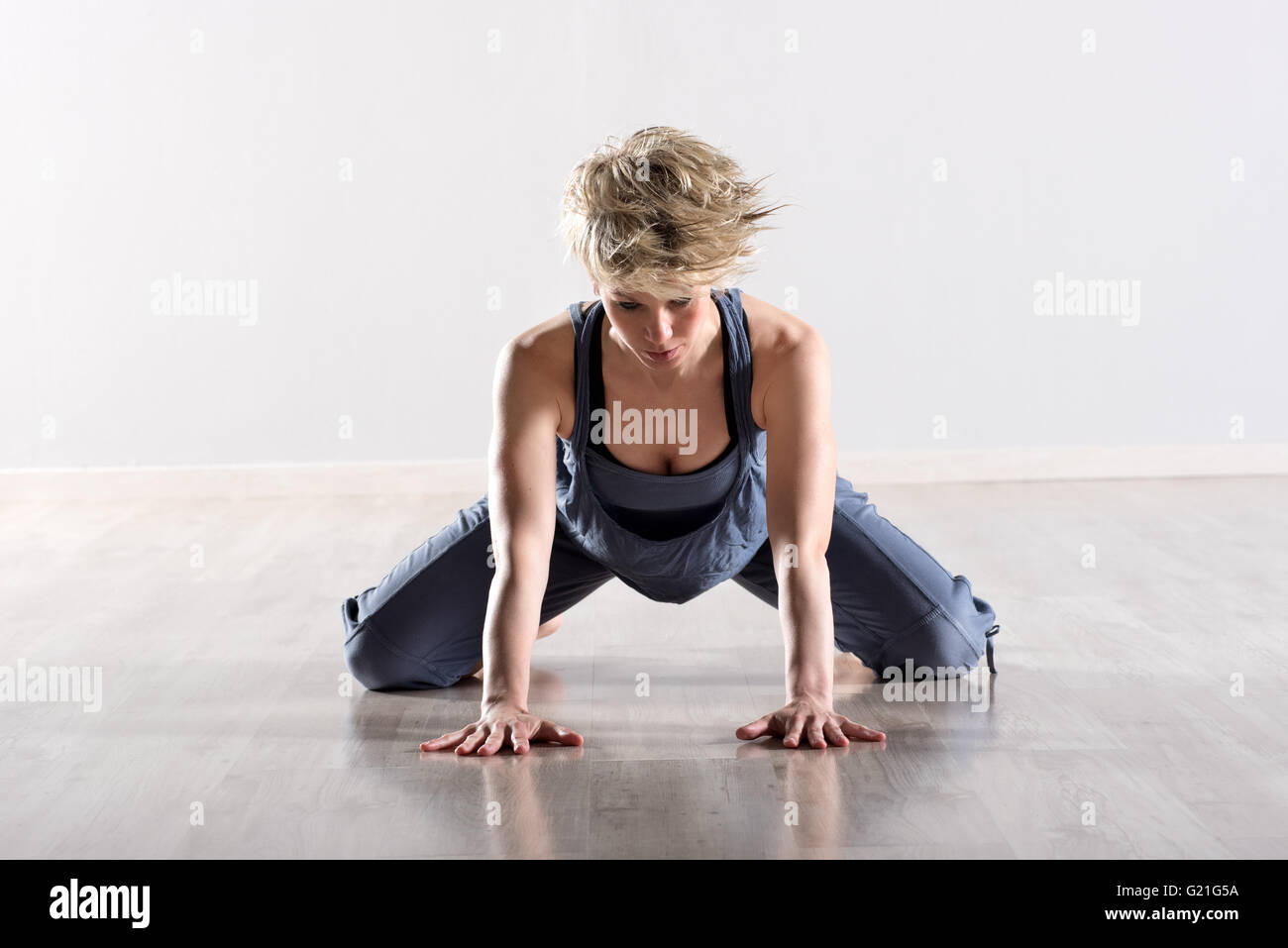 Sportliche blonde Yoga üben Frau in blau dehnen ihre Hüften während des Einsetzens Hände auf Parkett Stockfoto