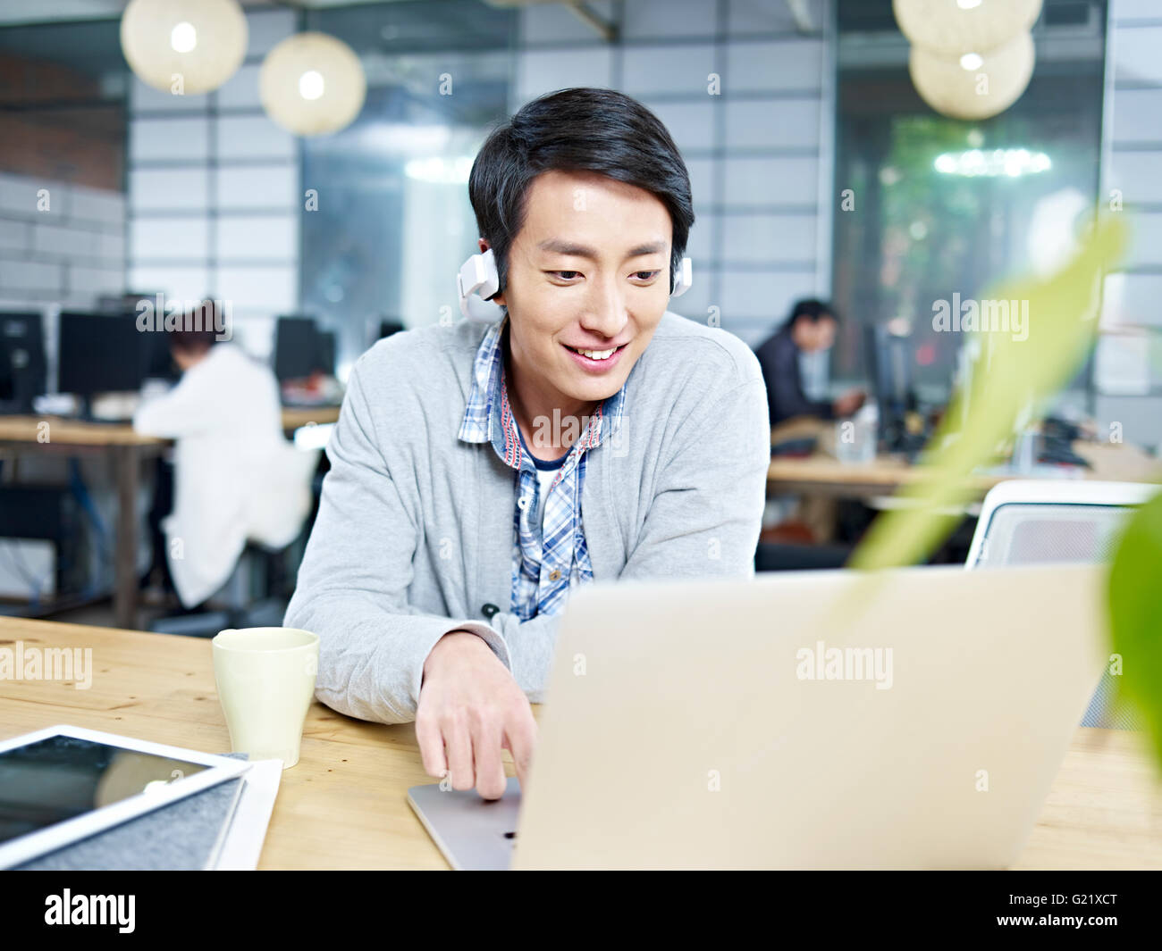 junge asiatische Mann arbeitet im Büro mit Kopfhörer Stockfoto