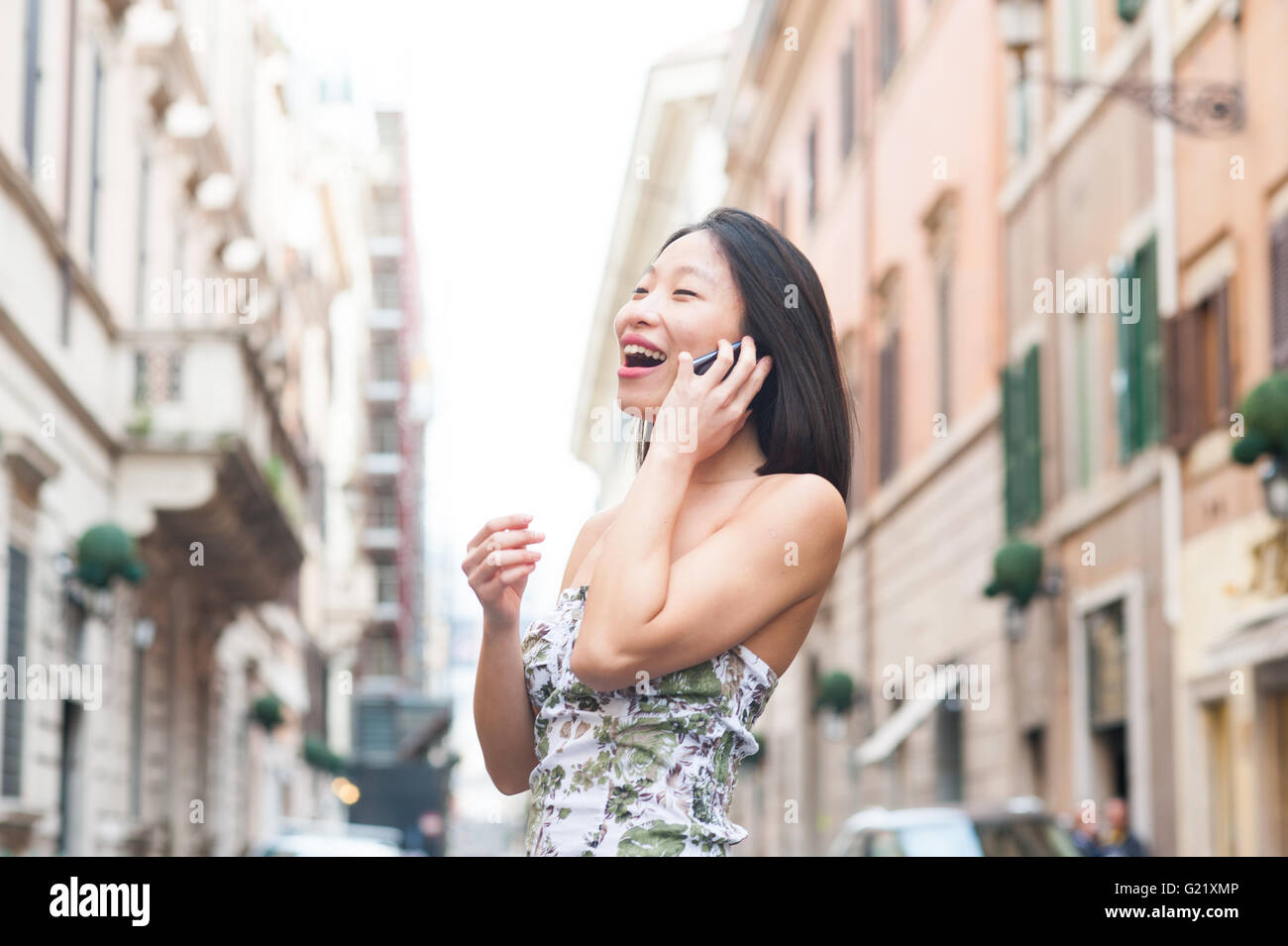 Junge schöne asiatische Frau lächelt Taliking am Handy auf der Straße Stockfoto