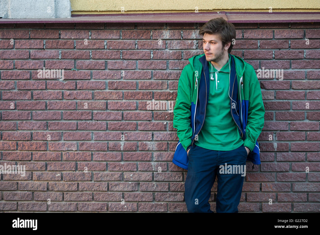 Gemeinsamen junger Mann trägt grün-t-Shirt-Jacke und Jeans gegen eine rote Mauer schauen seitwärts Stockfoto