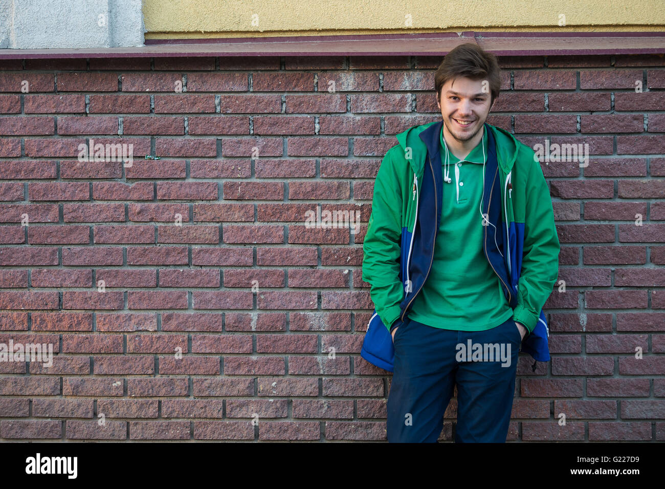 Gemeinsamen junger Mann trägt grün-t-Shirt-Jacke und Jeans gegen eine rote Mauer auf die Kamera Stockfoto