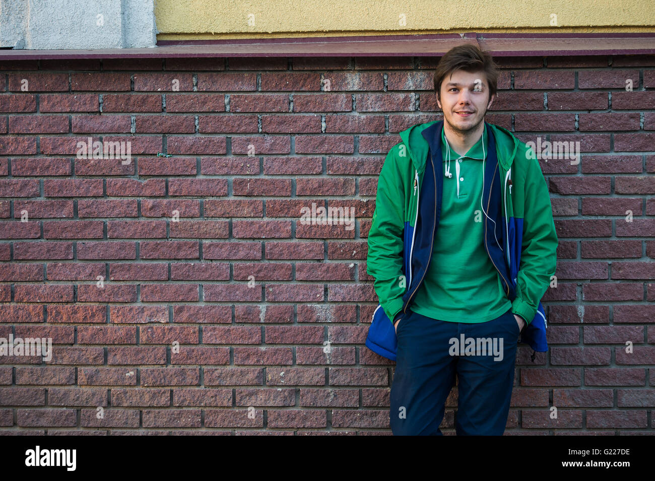 Gemeinsamen junger Mann trägt grün-t-Shirt-Jacke und Jeans gegen eine rote Mauer auf die Kamera Stockfoto