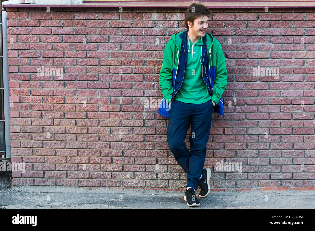 Gemeinsamen junger Mann trägt grün-t-Shirt-Jacke und Jeans gegen eine rote Mauer schauen seitwärts Stockfoto