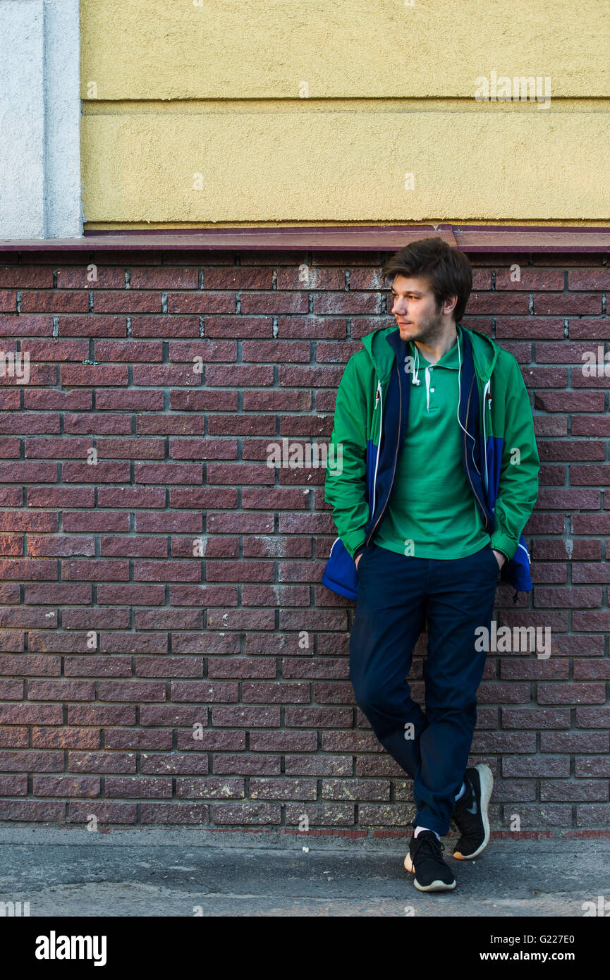 Gemeinsamen junger Mann trägt grün-t-Shirt-Jacke und Jeans gegen eine rote Mauer schauen seitwärts Stockfoto
