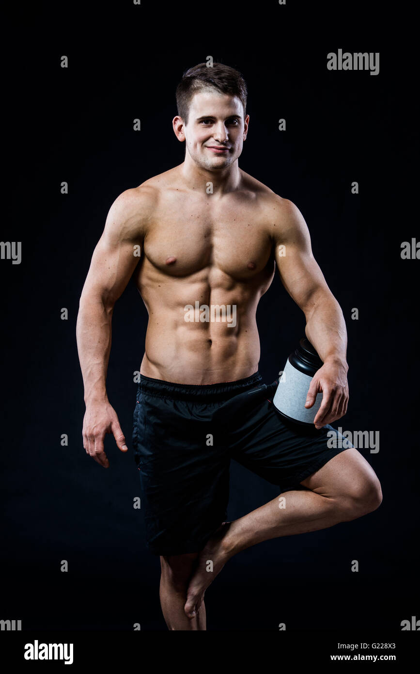 Bodybuilding und Sport Thema: schön stark Bodybuilder halten Kunststoff-Glas mit einem trockenen Protein Gefühl entspannt isolierten auf schwarzen Hintergrund im Studio Stockfoto