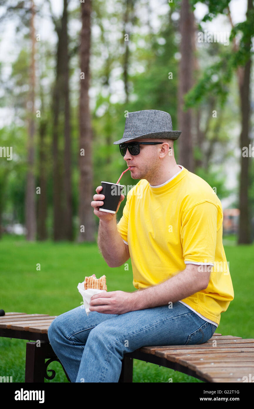 Mann mit Hut mit Kaffee und Sandwich auf Parkbank Stockfoto