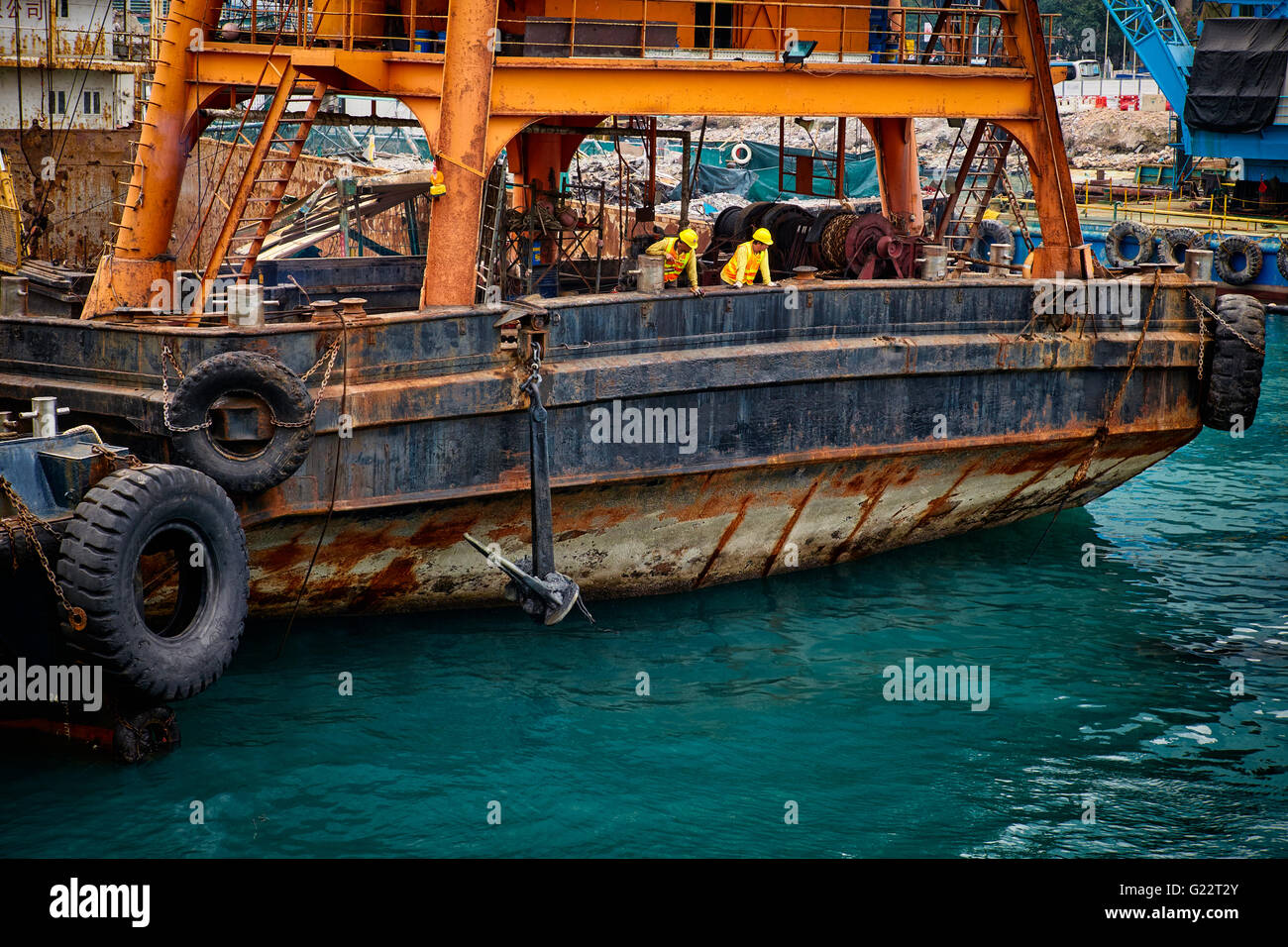 Zwei Arbeiter auf einem großen Schiff zu inspizieren die Gewässer rund um die Arbeit, die sie im Victoria Harbour, Hongkong tun. Stockfoto