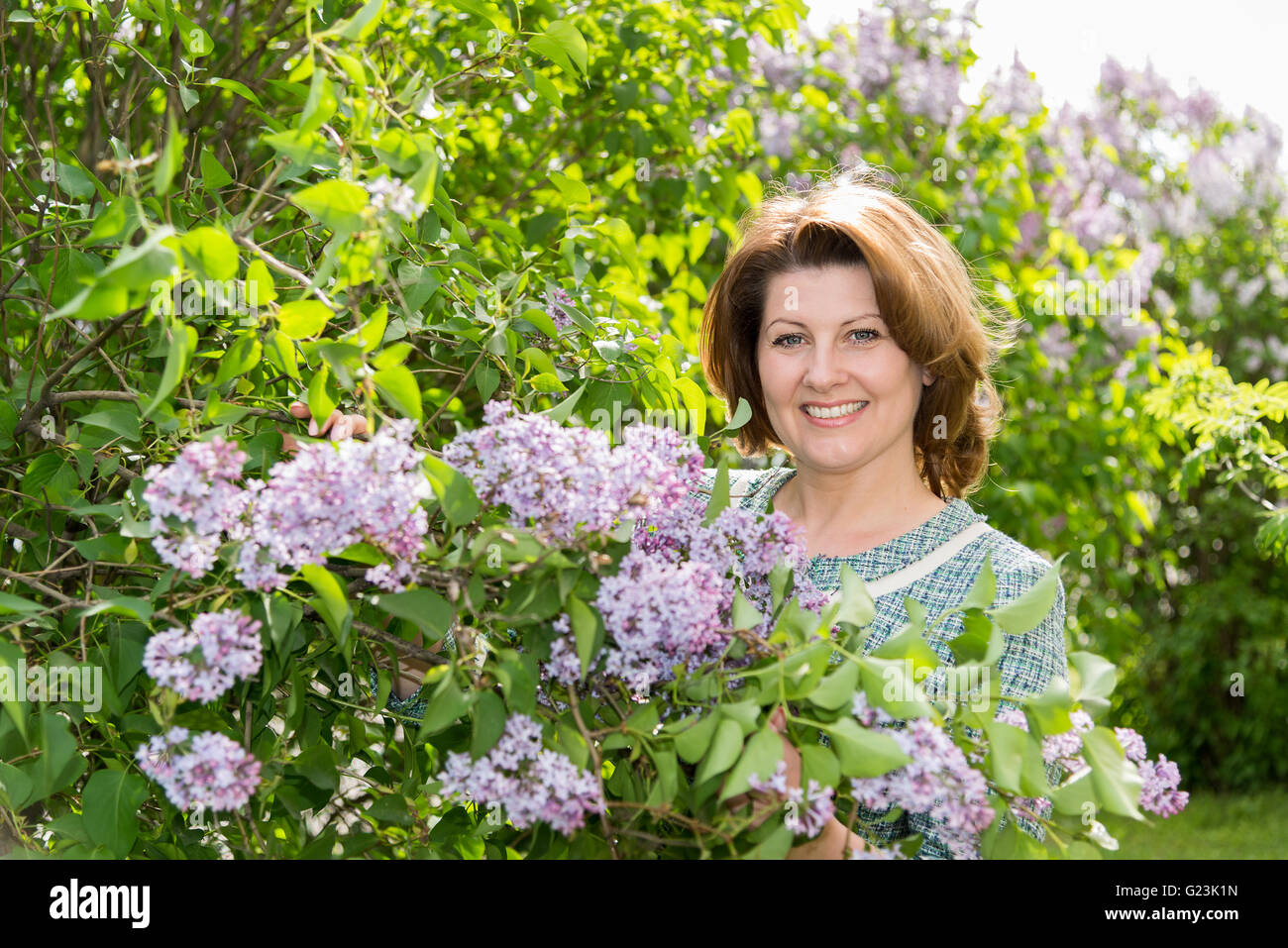 Erwachsene Frau im Park in der Nähe der blühenden Flieder Stockfoto