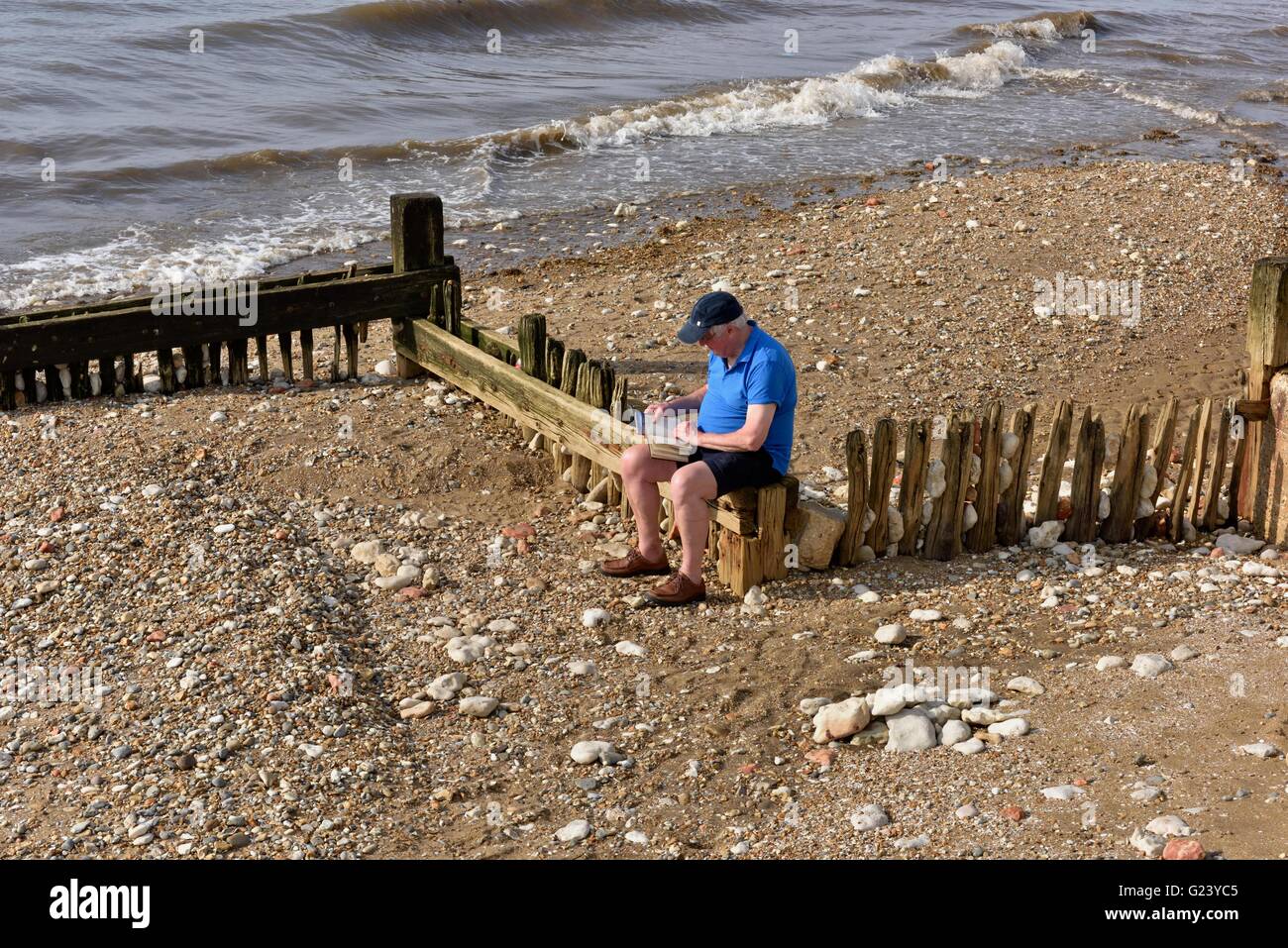 Älteren Senior Mann sitzen, ein Buch lesen auf Hunstanton Beach Norfolk England UK Stockfoto