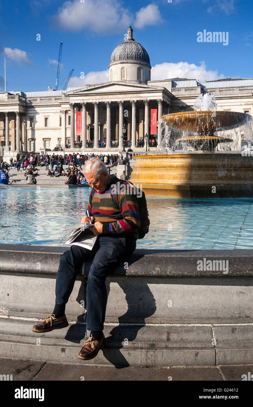 Ein Mann sitzt schreiben am Rande Brunnen vor der National Gallery, Trafalgar Square, London, England Stockfoto