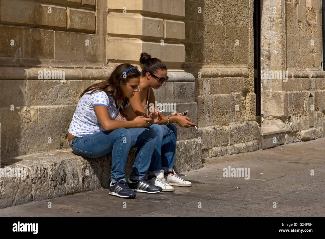 Zwei Mädchen in ihren mobilen absorbiert "Handys und Zigaretten, Piazza del Duomo, Lecce, Apulien, Italien Stockfoto