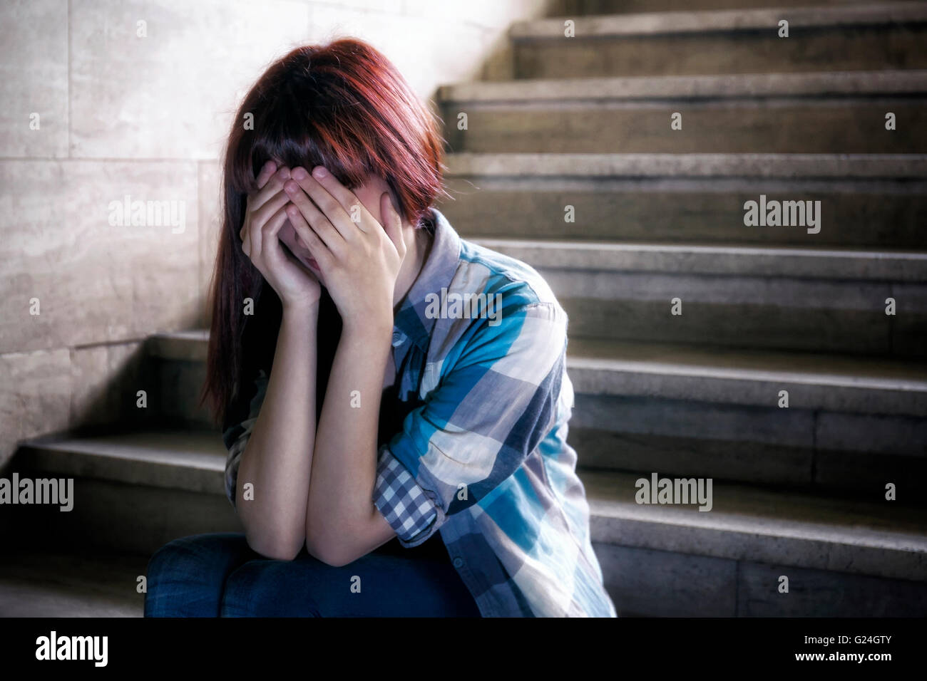 Mädchen in der Adoleszenzkrise sitzen auf den Stufen der Keller, erstreckt sich ihr Gesicht mit den Händen. Ein natürliches Licht dringt von ab Stockfoto