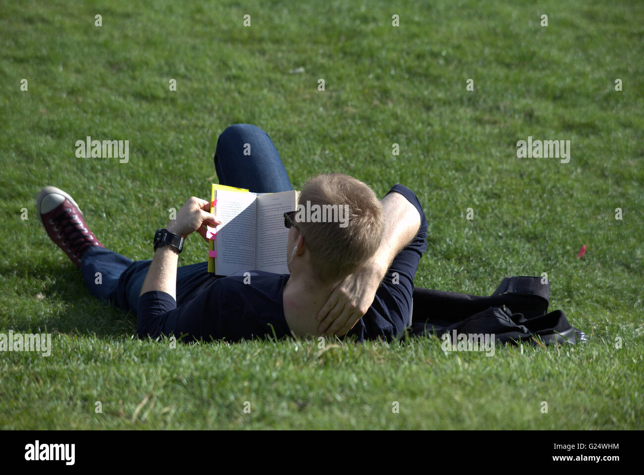 Mann oder ein Junge am Rasen Lesebuch im Kelvingrove Park Glasgow, Scotland, UK liegen. Stockfoto