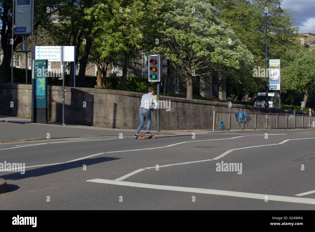 Junger Mann skateboarding eine Straße vorbei an Ampeln auf grün für Go Glasgow, Schottland, UK. Stockfoto