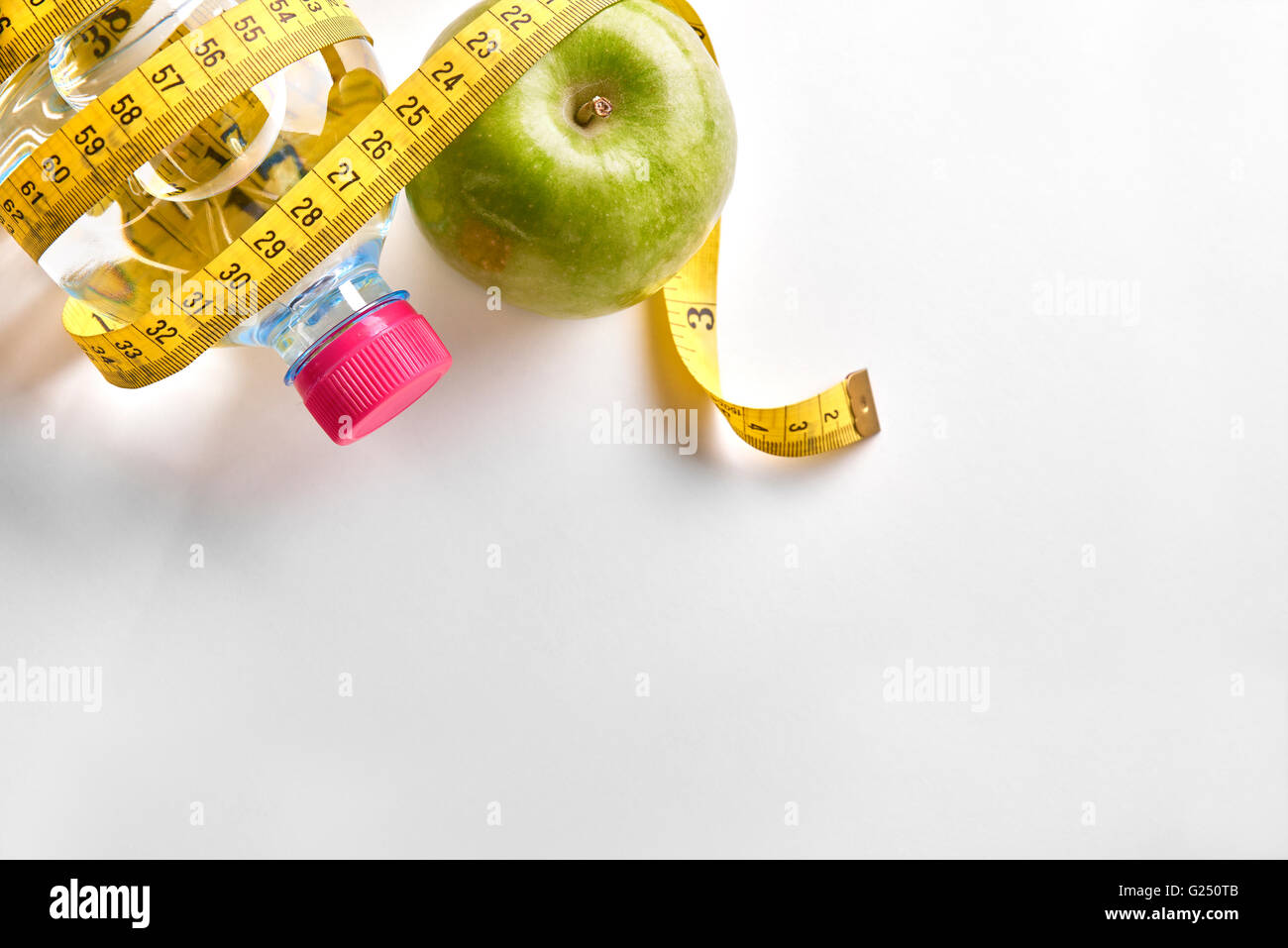 Maßband um eine Flasche Mineralwasser und Apfel auf weißen Tisch. Konzept Gesundheit, Diät und Ernährung. Stockfoto