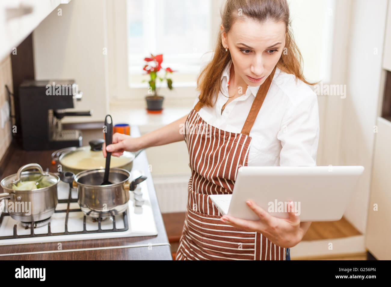 Junge Frau, die versucht, Kochen mit Rezept von Laptop. Schockiert, Kaukasische Frau online-lernen kochen Stockfoto