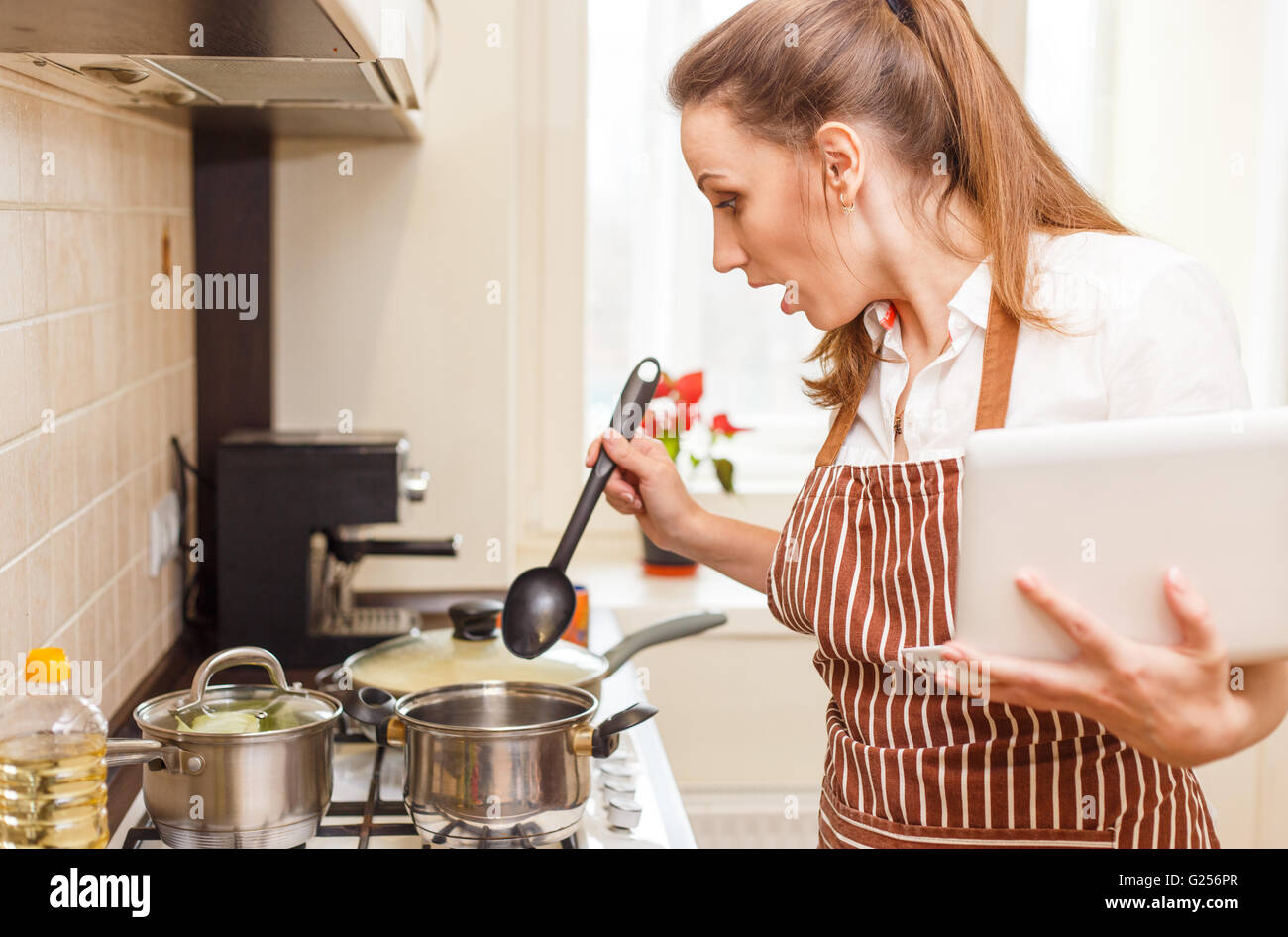 Junge Frau, die versucht, Kochen mit Rezept von Laptop. Schockiert, Kaukasische Frau online-lernen kochen Stockfoto