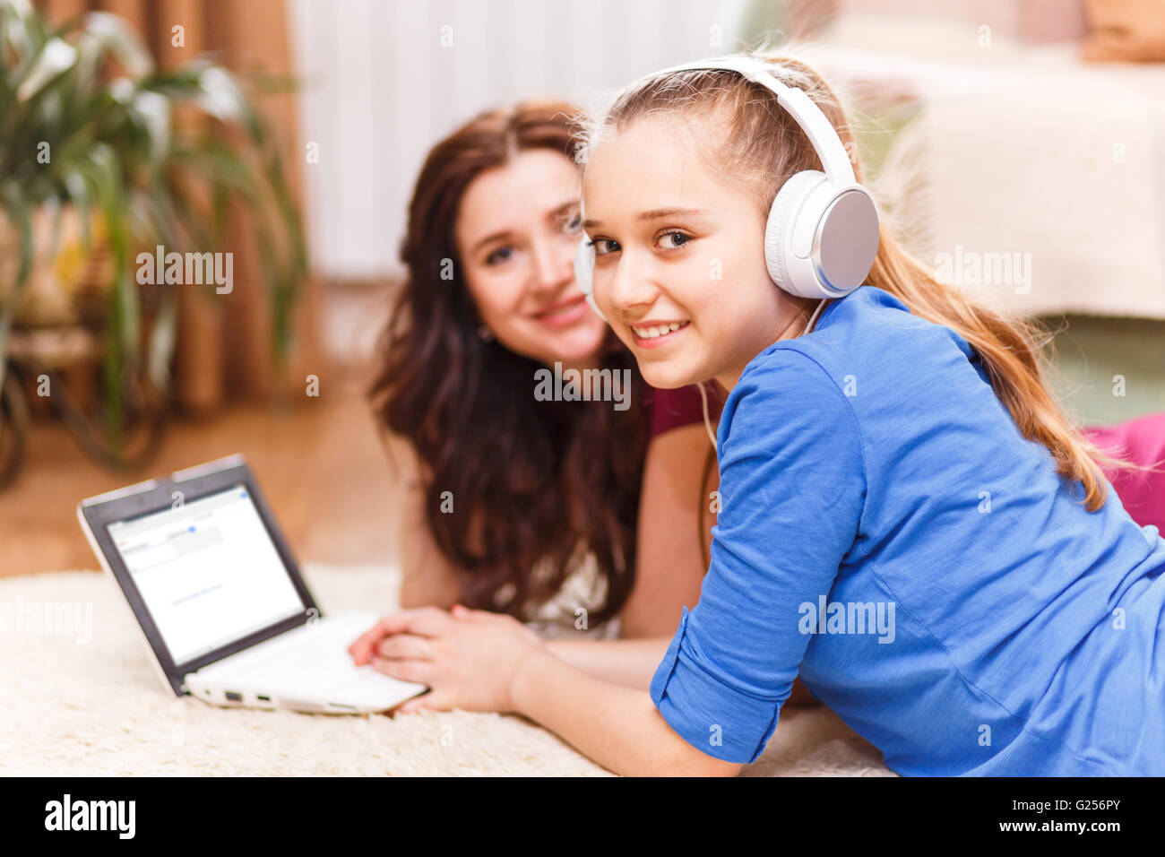 Teenager-Mädchen in Kopfhörer mit Laptop mit ihrer Mutter auf dem Boden liegend. Zeit mit der Familie zusammen Stockfoto