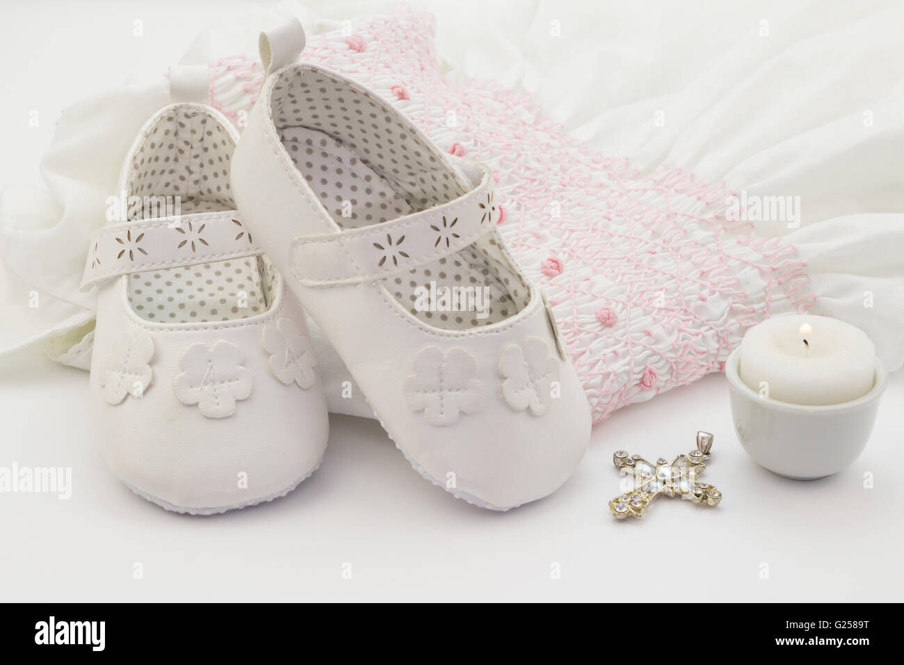 Weiße Baby Schuhe auf weißen bestickt Taufe Kleid, Kreuz und Kerze  Stockfotografie - Alamy
