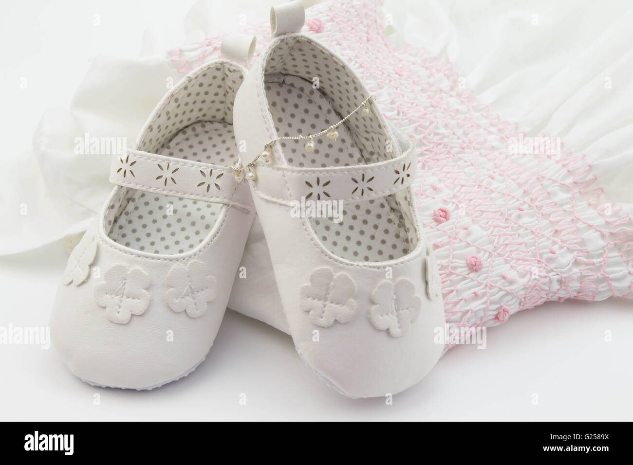 Weiße Baby Schuhe auf bestickten weißen und rosa Kleid und Perlenarmband Stockfoto