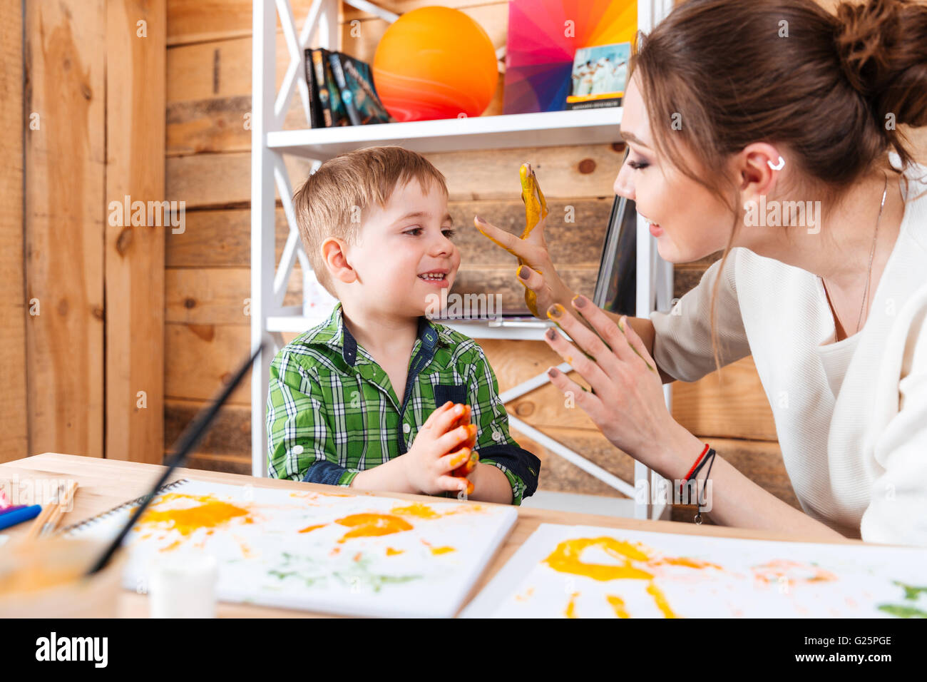 Niedlichen kleinen Jungen und seiner Mutter sitzen und Spaß mit ihren bemalten Händen in bunten Farben Stockfoto