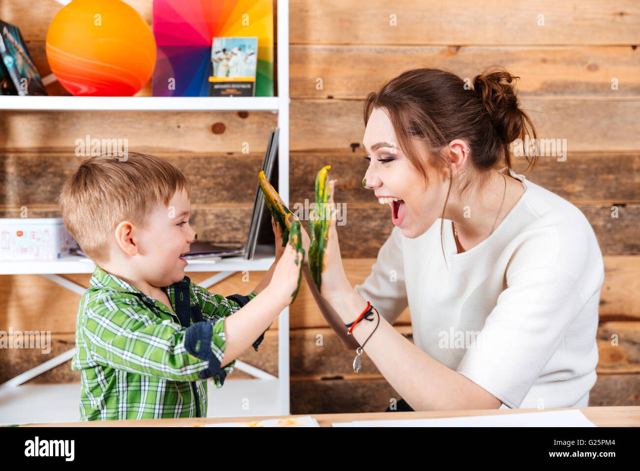 Glückliche junge Mutter und ihr kleiner Sohn geben hohe fünf mit bemalten Händen in bunten Farben Stockfoto